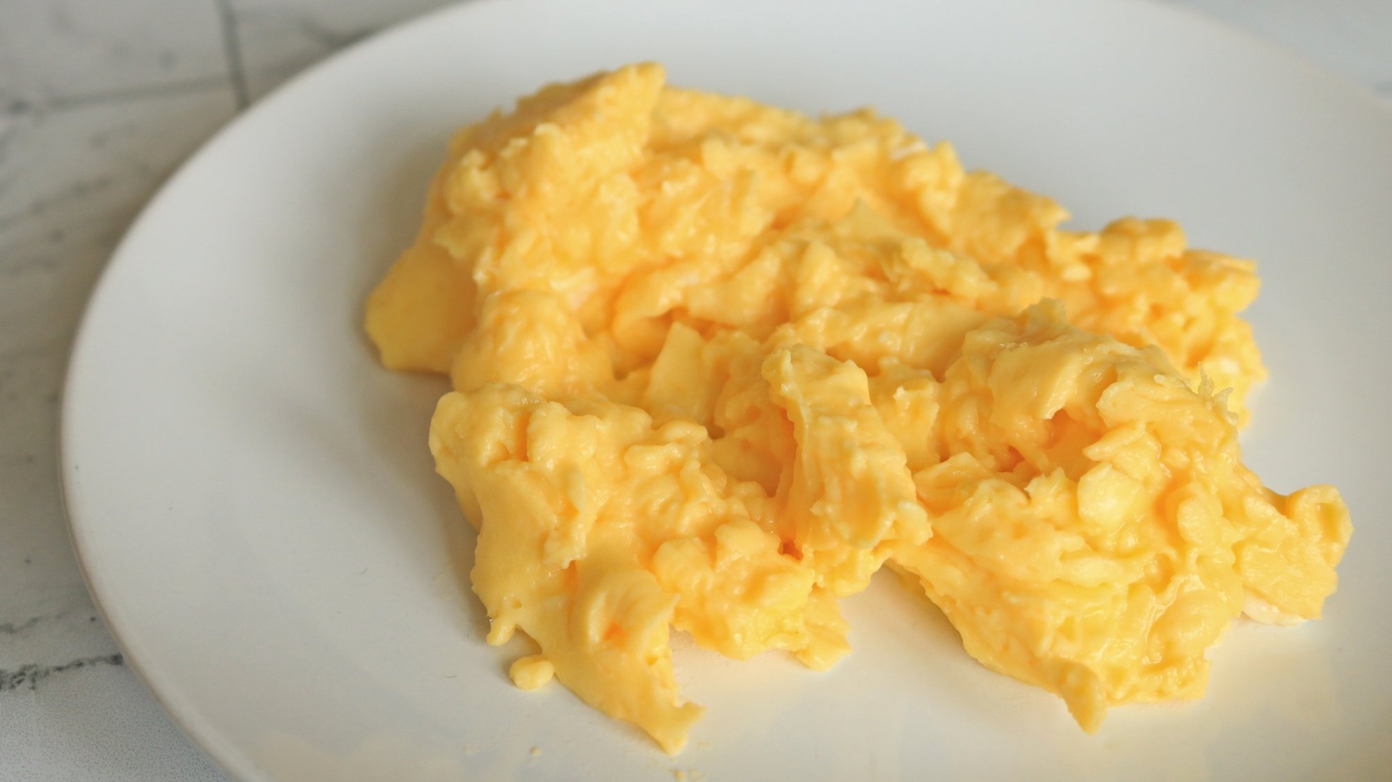 Fork-scrambled eggs on a white plate.