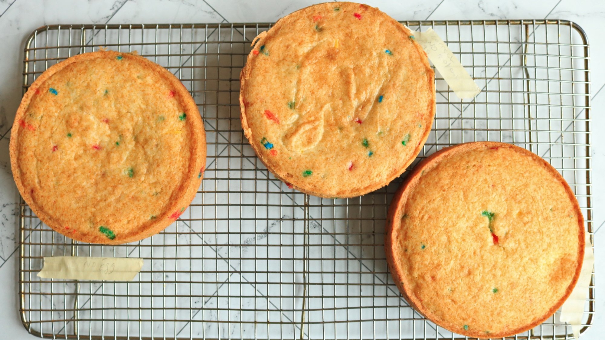 Three layers of funfetti cake on a wire cooling rack.