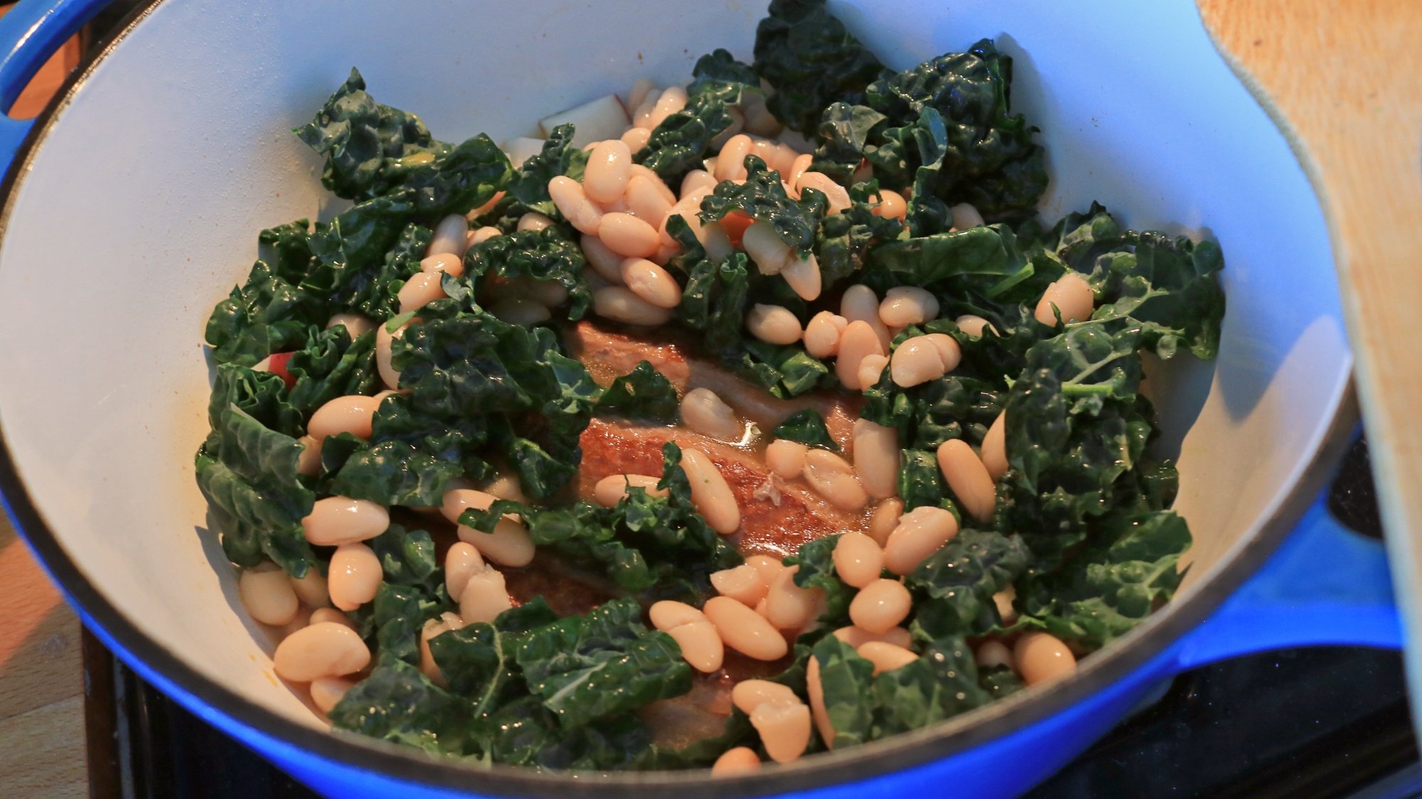 Kale, beans, and sausage in a Dutch oven.