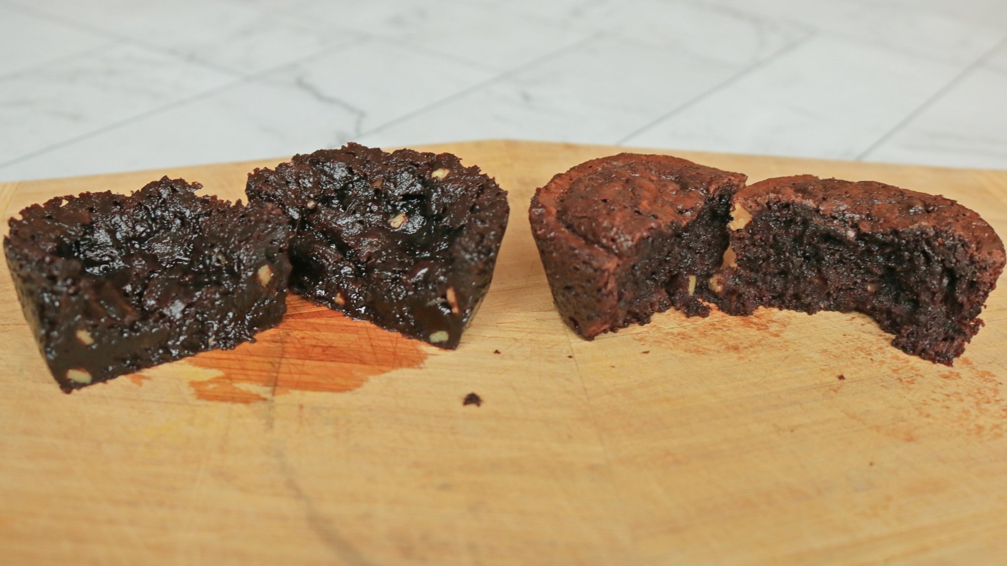 One greasy and dark brown brownie bite next to a lighter brown and fluffy brownie bite.