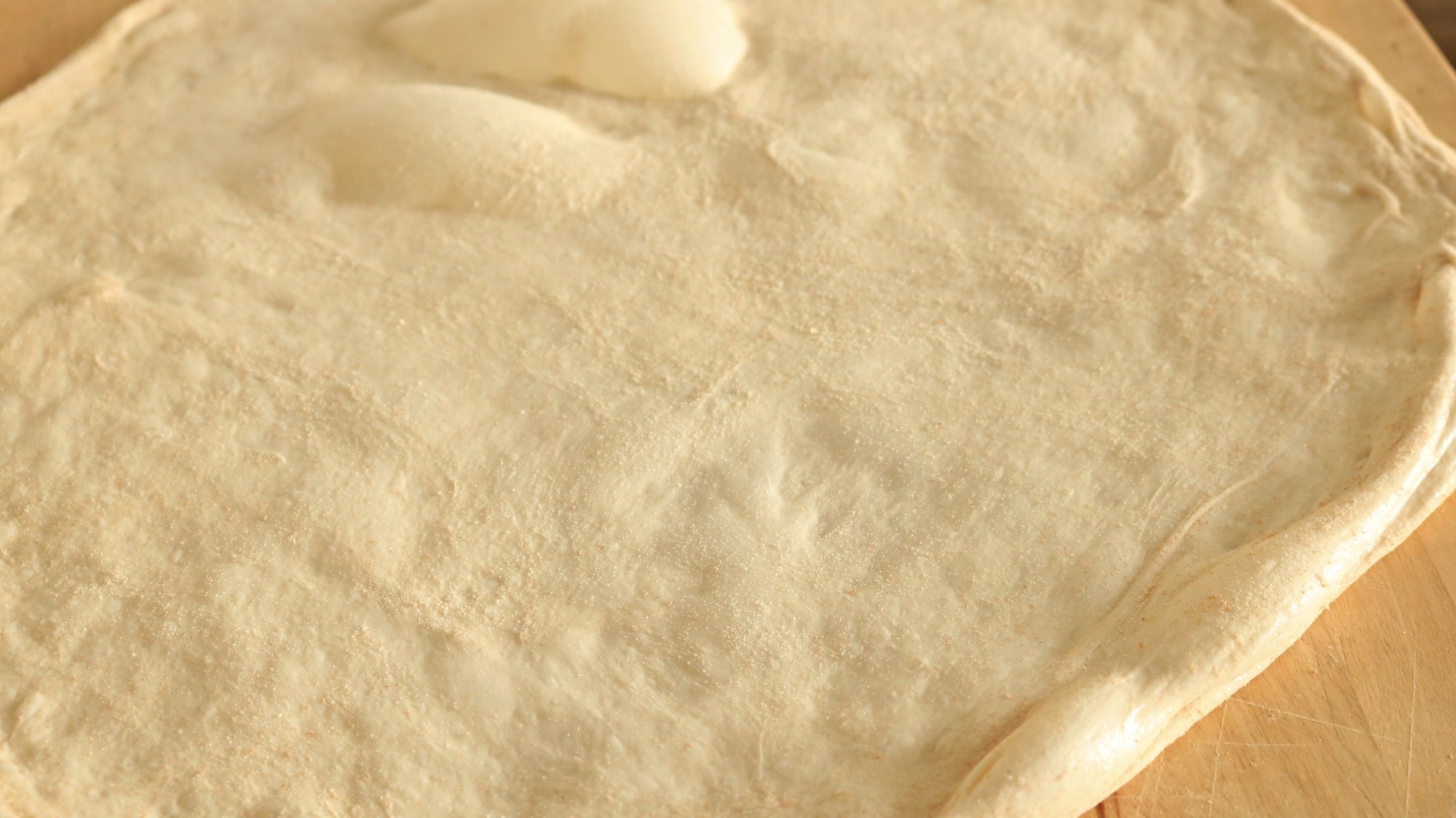 Stretched out pizza dough with bubbles.