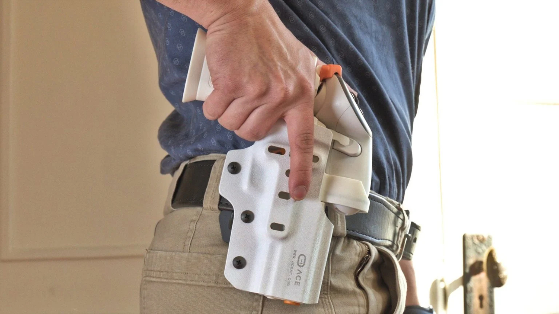 Person in blue shirt pulling dummy handgun from white Kydex holster with orange controls on tactical belt.