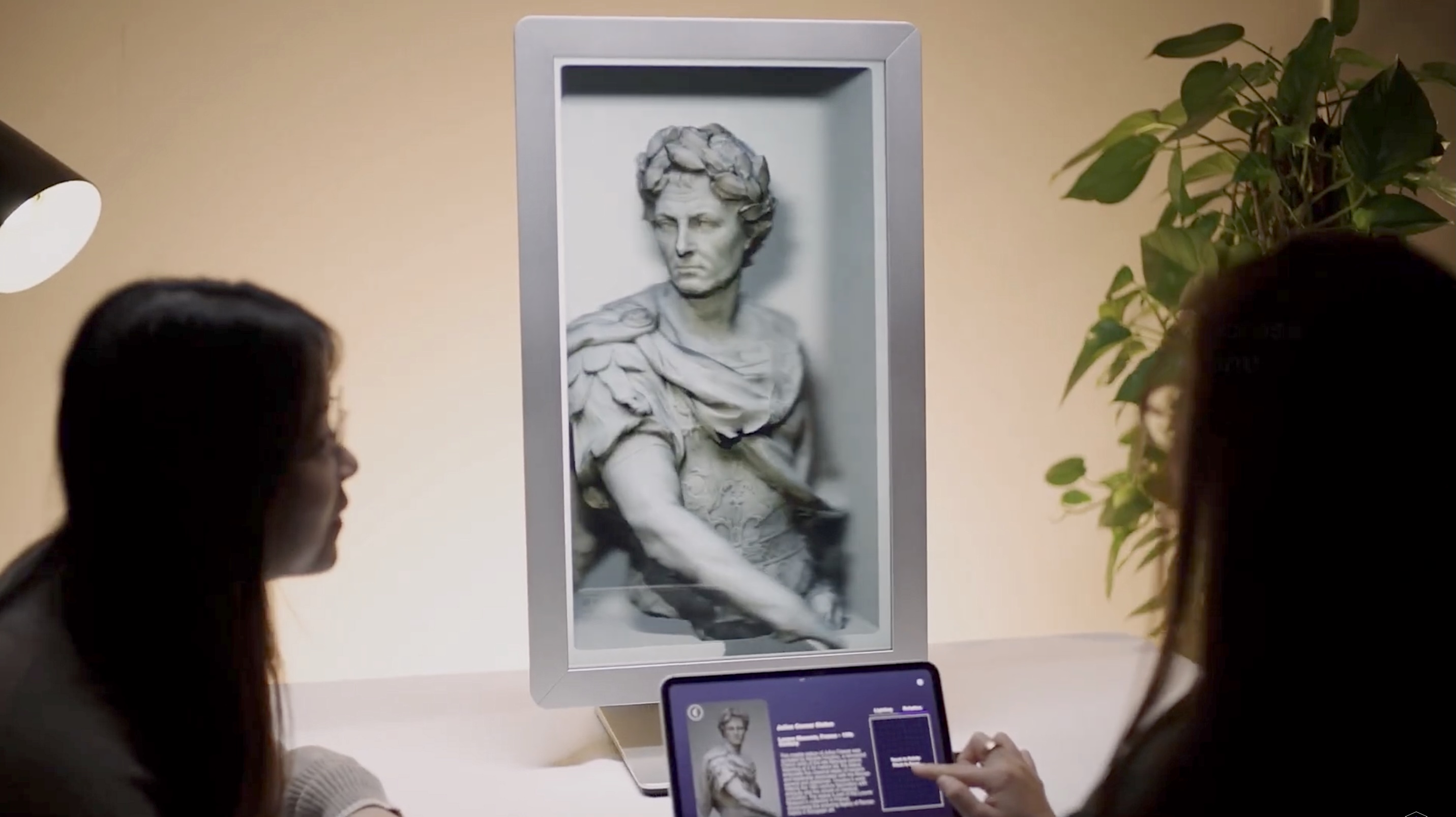 Digital 3D image of a Roman bust, viewed by two people. One person controls the display via a tablet.