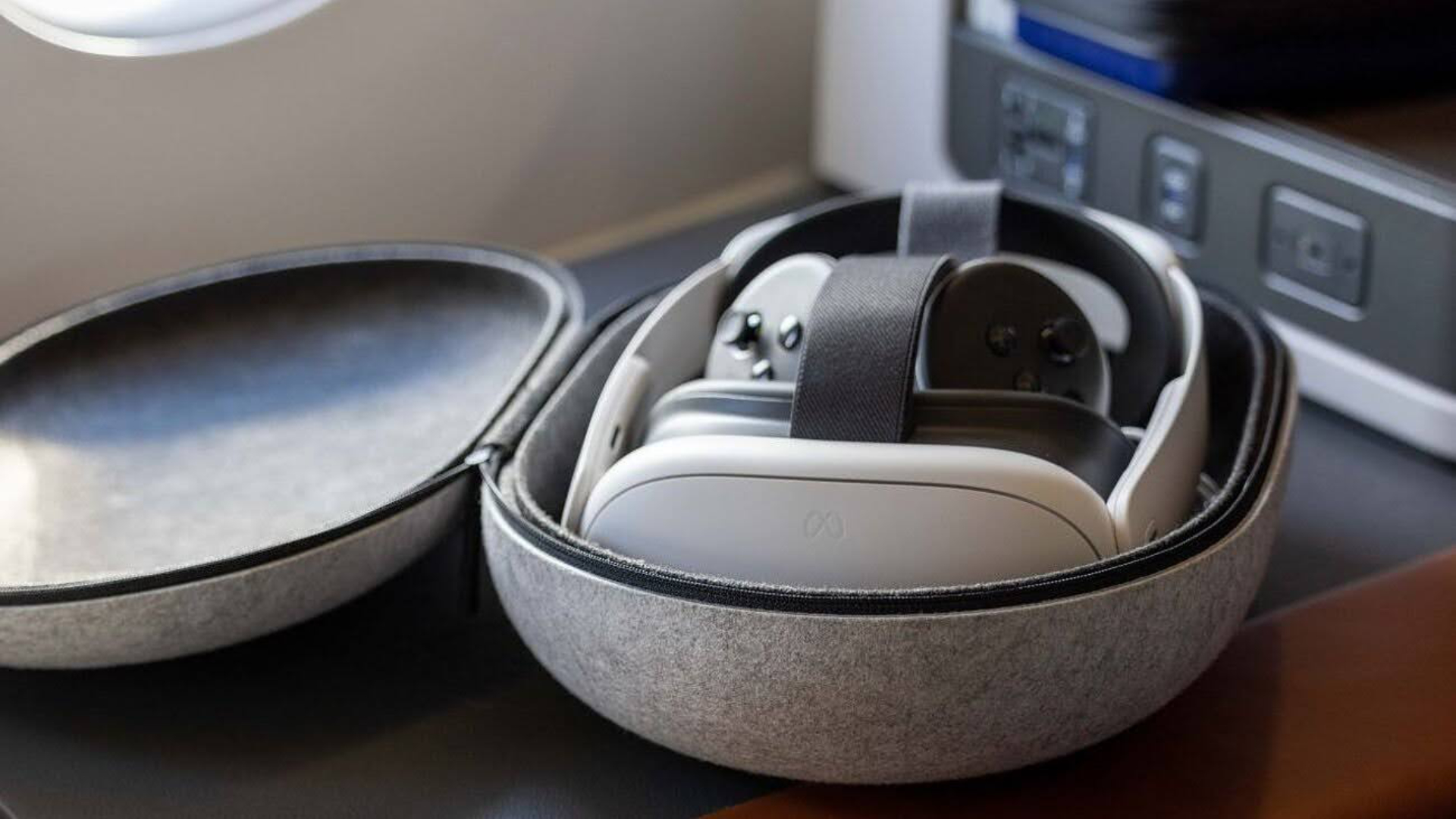 [ALT-TEXT] White VR headset and controller in gray, open transport box, in the background a part of the aircraft interior.
