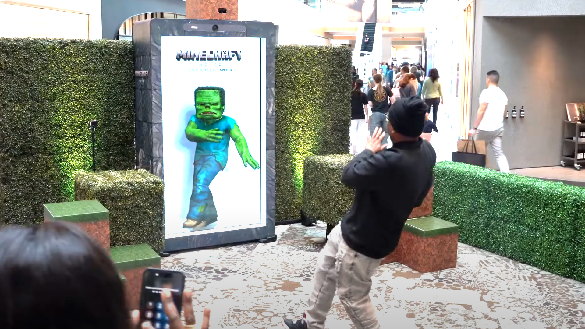Interactive Minecraft movie ad with digital zombie display, surrounded by green hedges and a visitor interacting with the installation.
