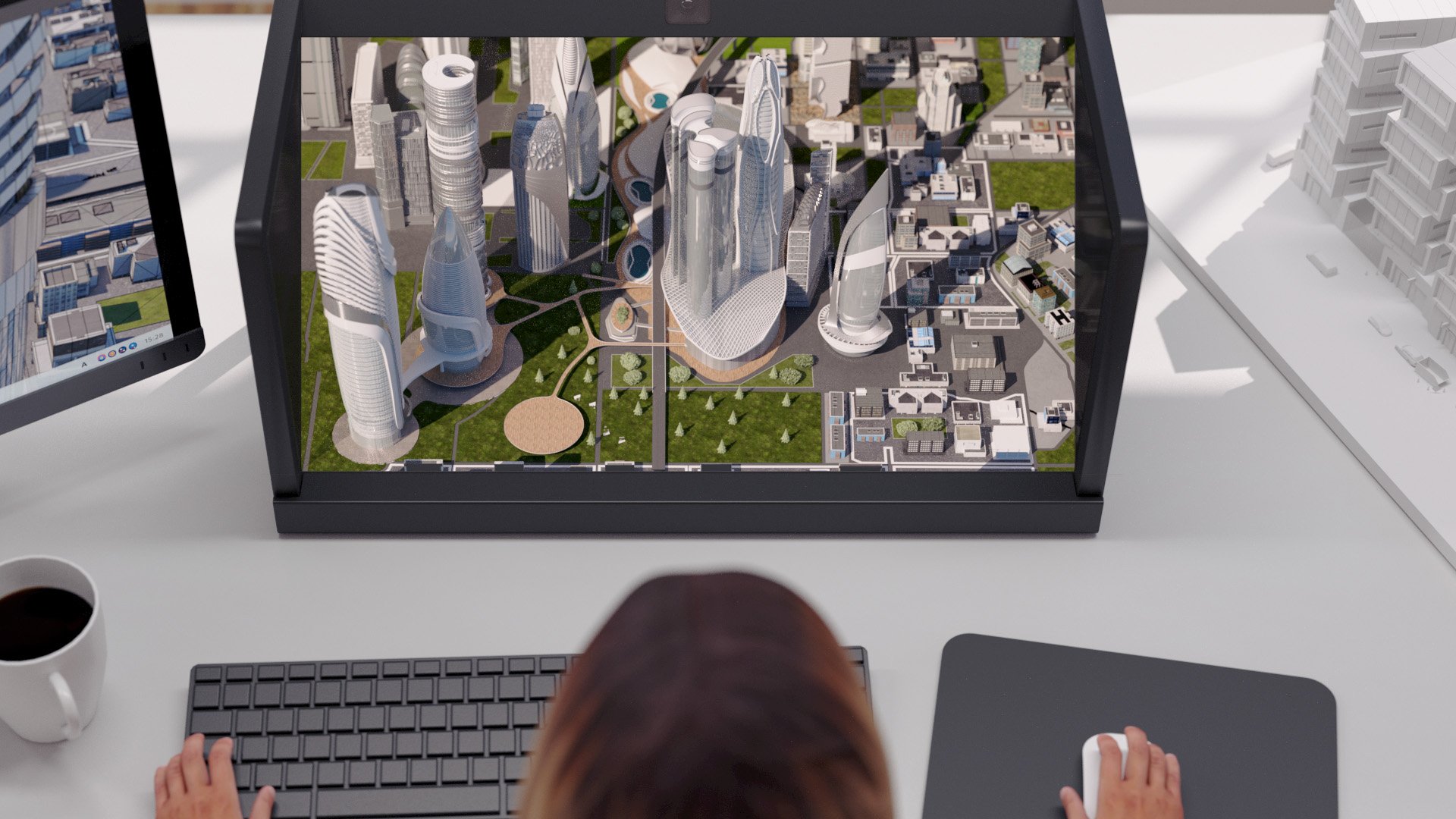 A person sits at a desk and looks at a 3D display showing urban architecture.