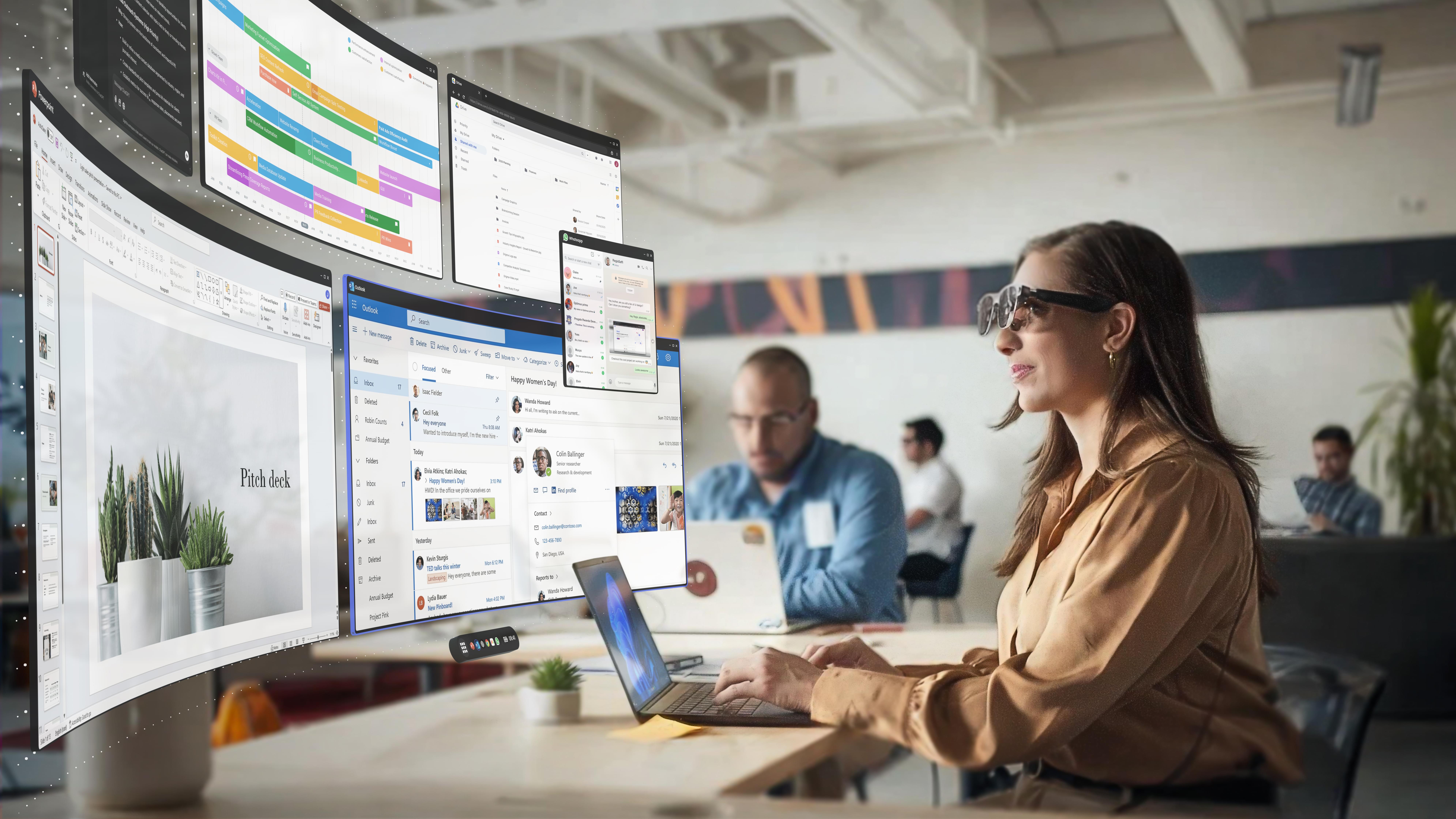 A woman wears an AR headset in an office and looks at a virtual multi-monitor setup.