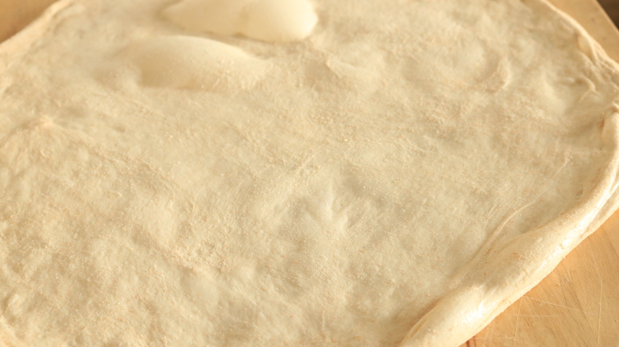 Raw pizza dough on a cutting board.