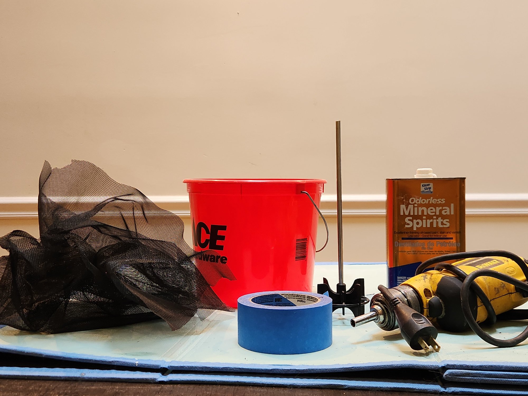 Fiberglass screen, bucket, painter's tape, paddle attachment, power drill, and mineral spirits.