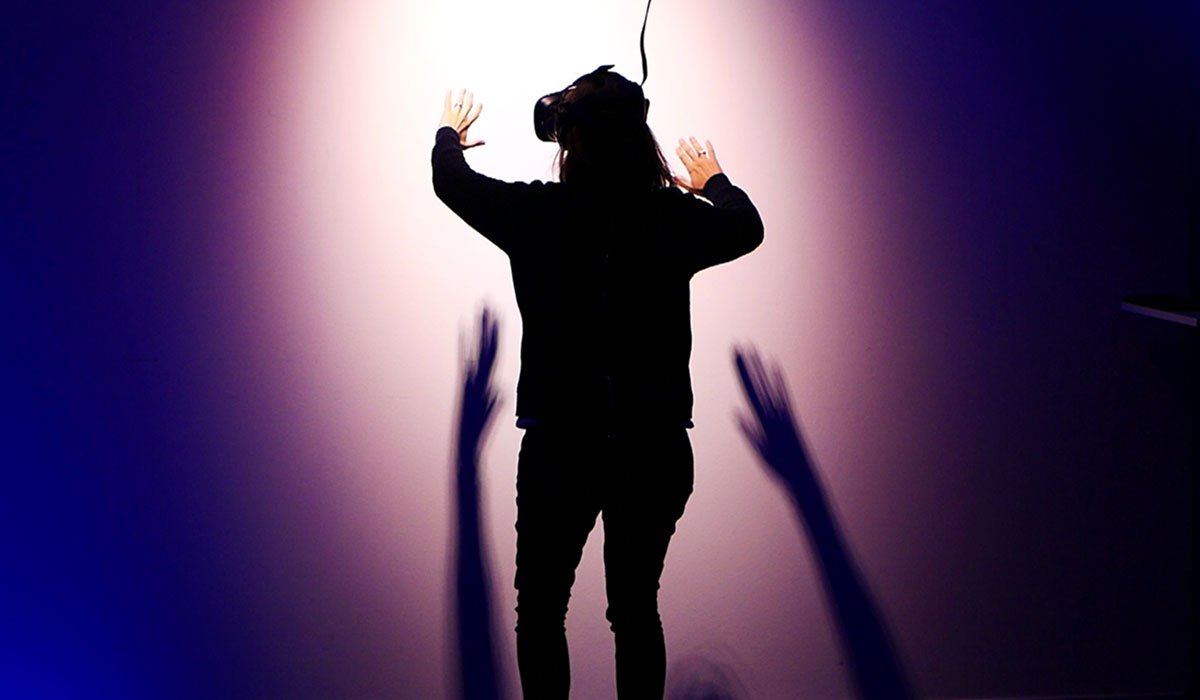 A woman with a VR headset stands in the room with a bright light in front of her.