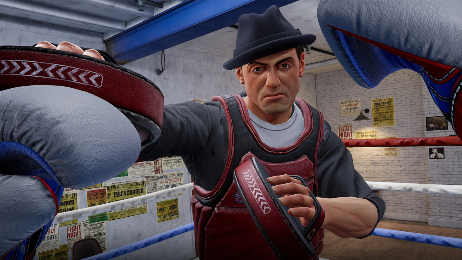Boxing trainer with hat and red punching pads in a boxing studio with boxing ring and posters in the background.