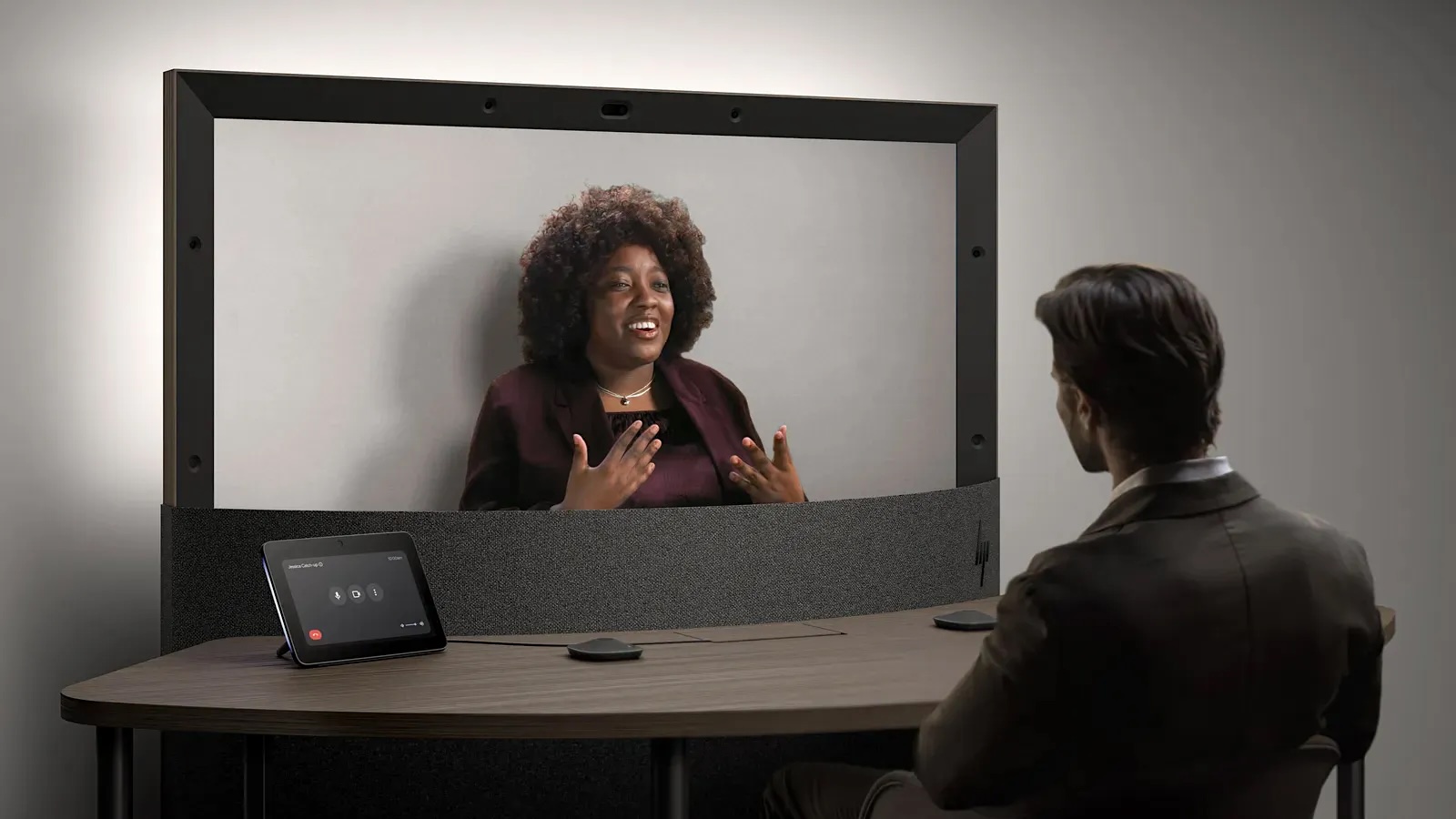 Beam video conferencing system with large screen, control tablet and person in business attire during a virtual meeting.