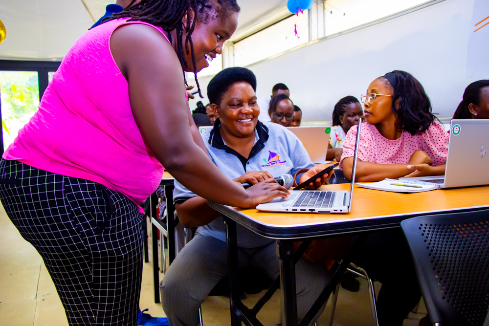 An educator helps students with a coding task in a classroom.