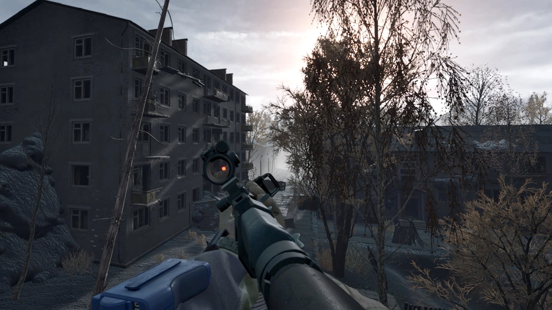 First-person shooter view with gun barrel, scope and red dot sight against a decaying city backdrop in dull daylight.
