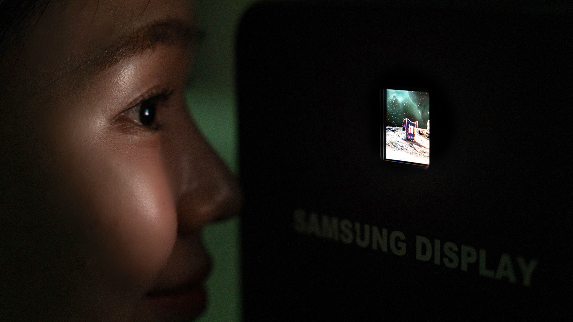 Close-up of a Samsung display in the dark with a glowing space scene and a futuristic object on the surface of the moon.