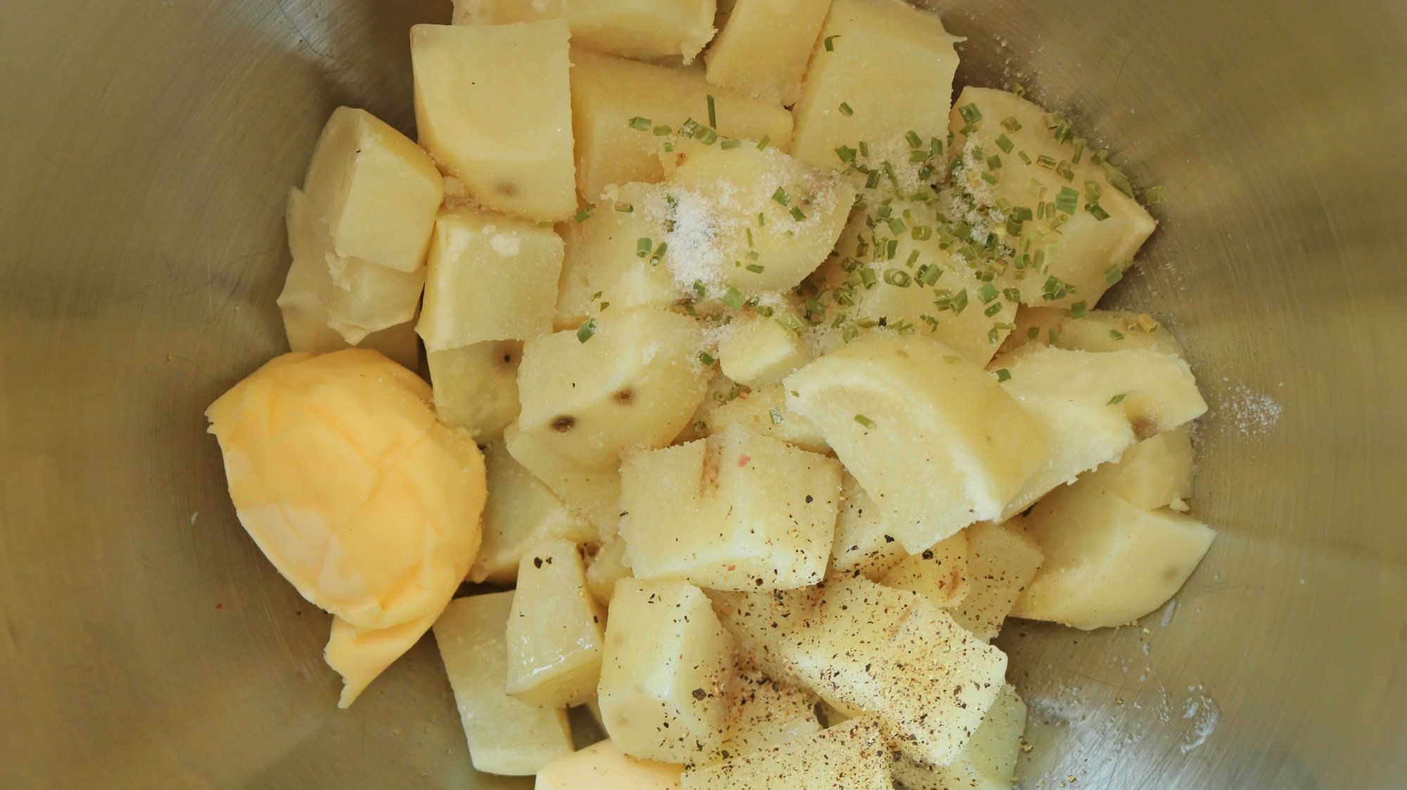 Cubed potatoes with butter and dry chives in a silver bowl.