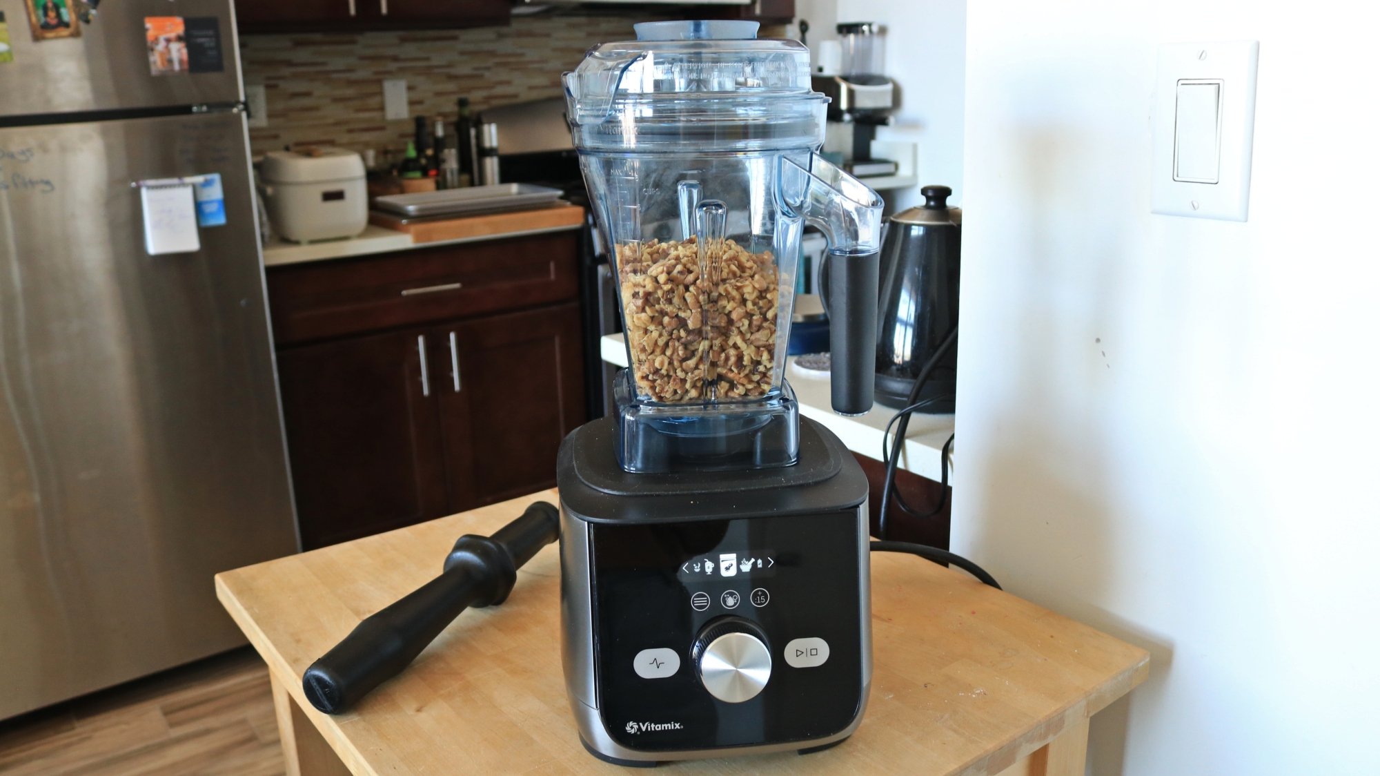 A blender with walnuts in the container in a kitchen.