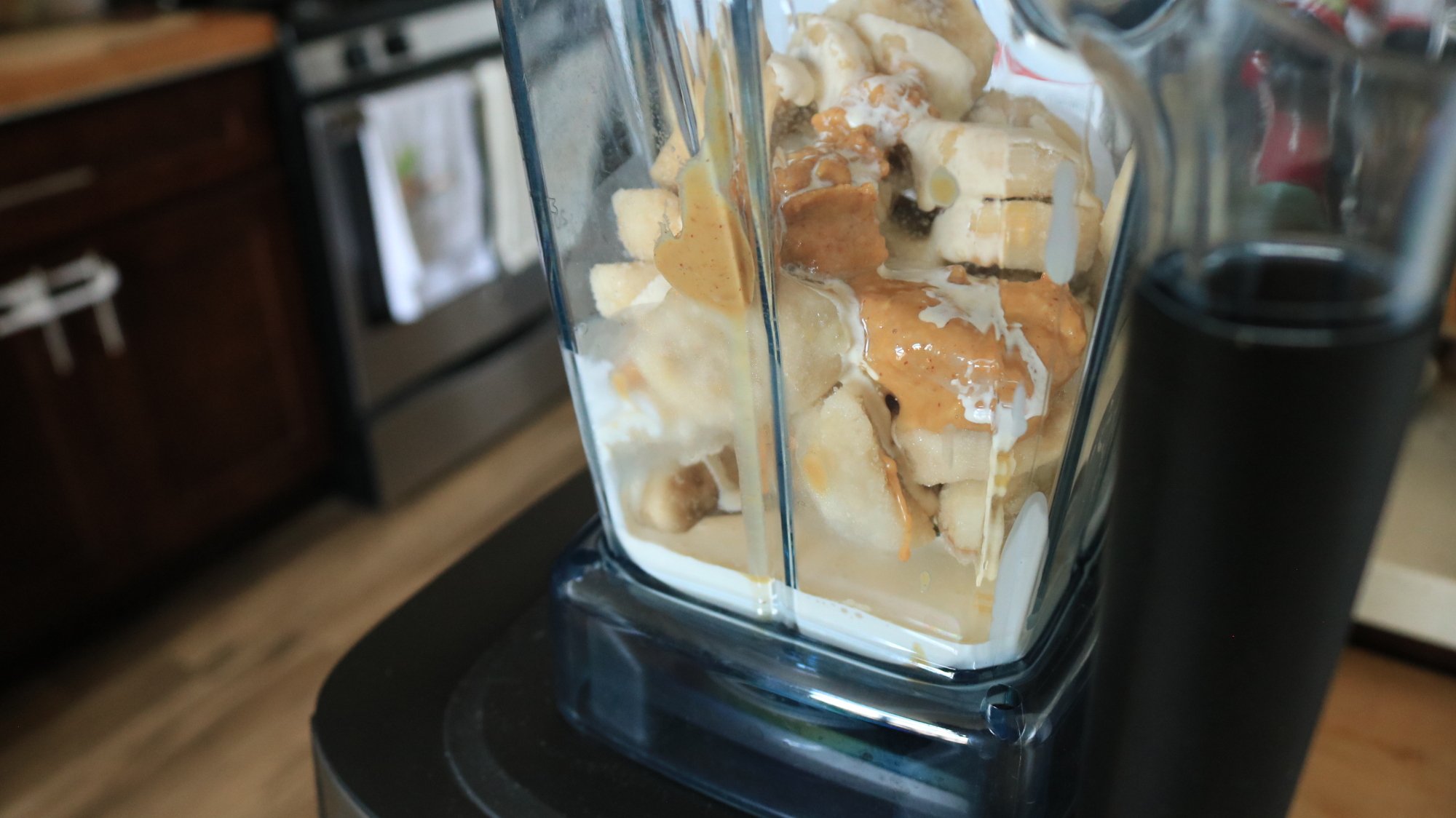 A Vitamix blender container with bananas, vegan cream, and peanut butter.