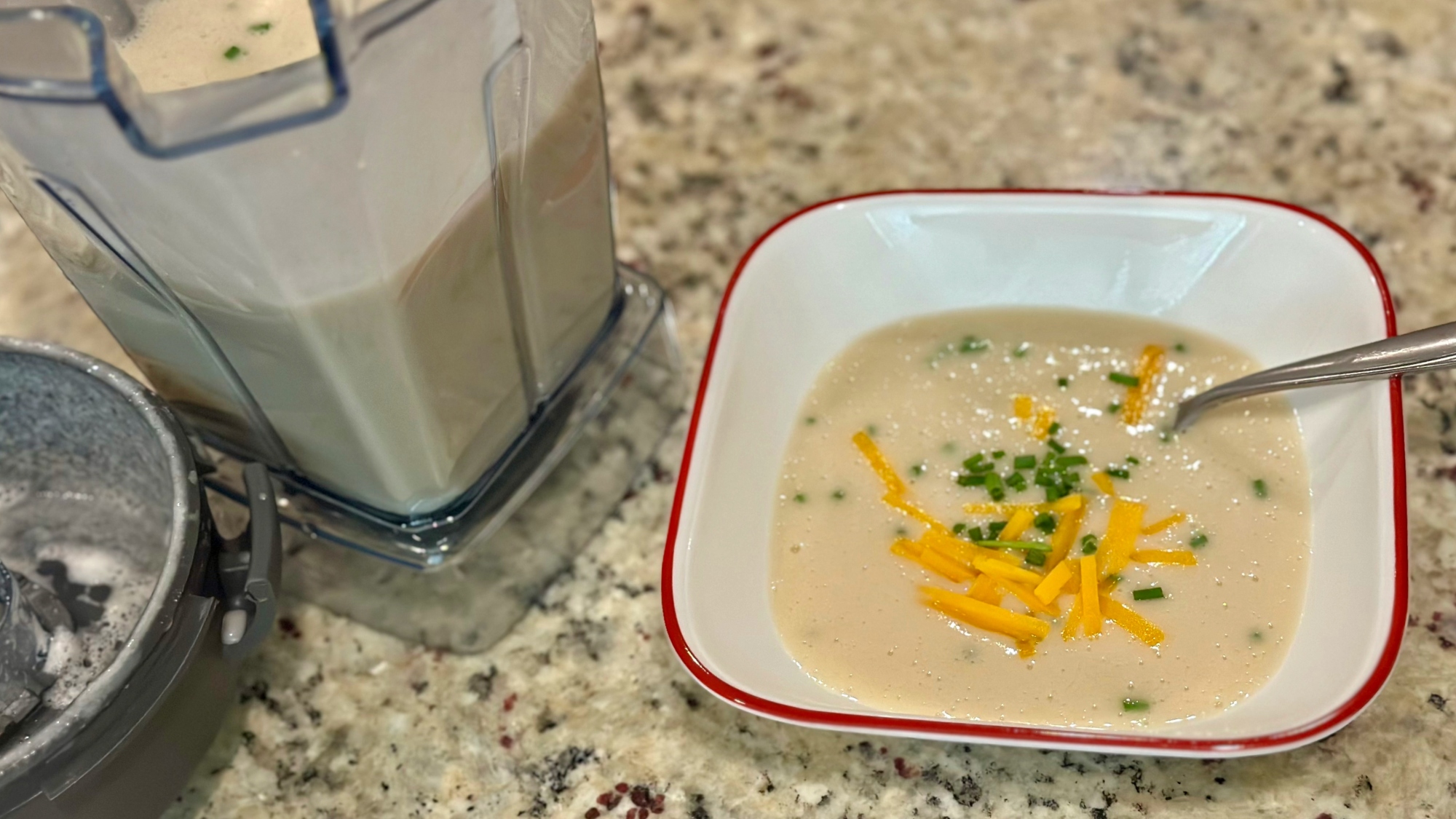 A bowl of potato soup next to a blender container.
