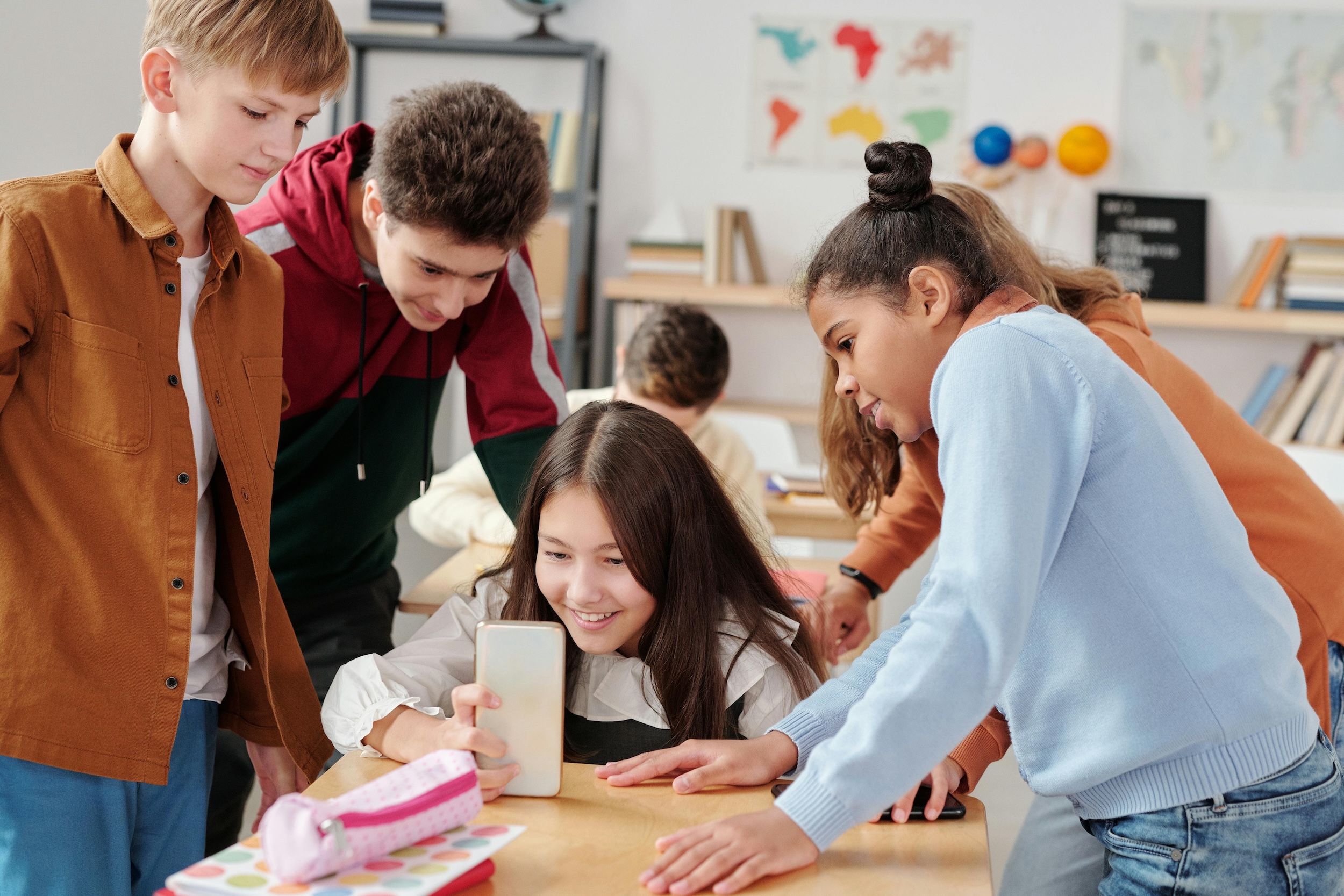 Photo of a young person in a classroom showing their phone screen to their friends.