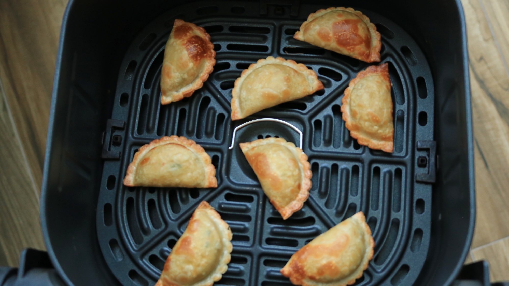 Dumplings spread out in an air fryer basket.