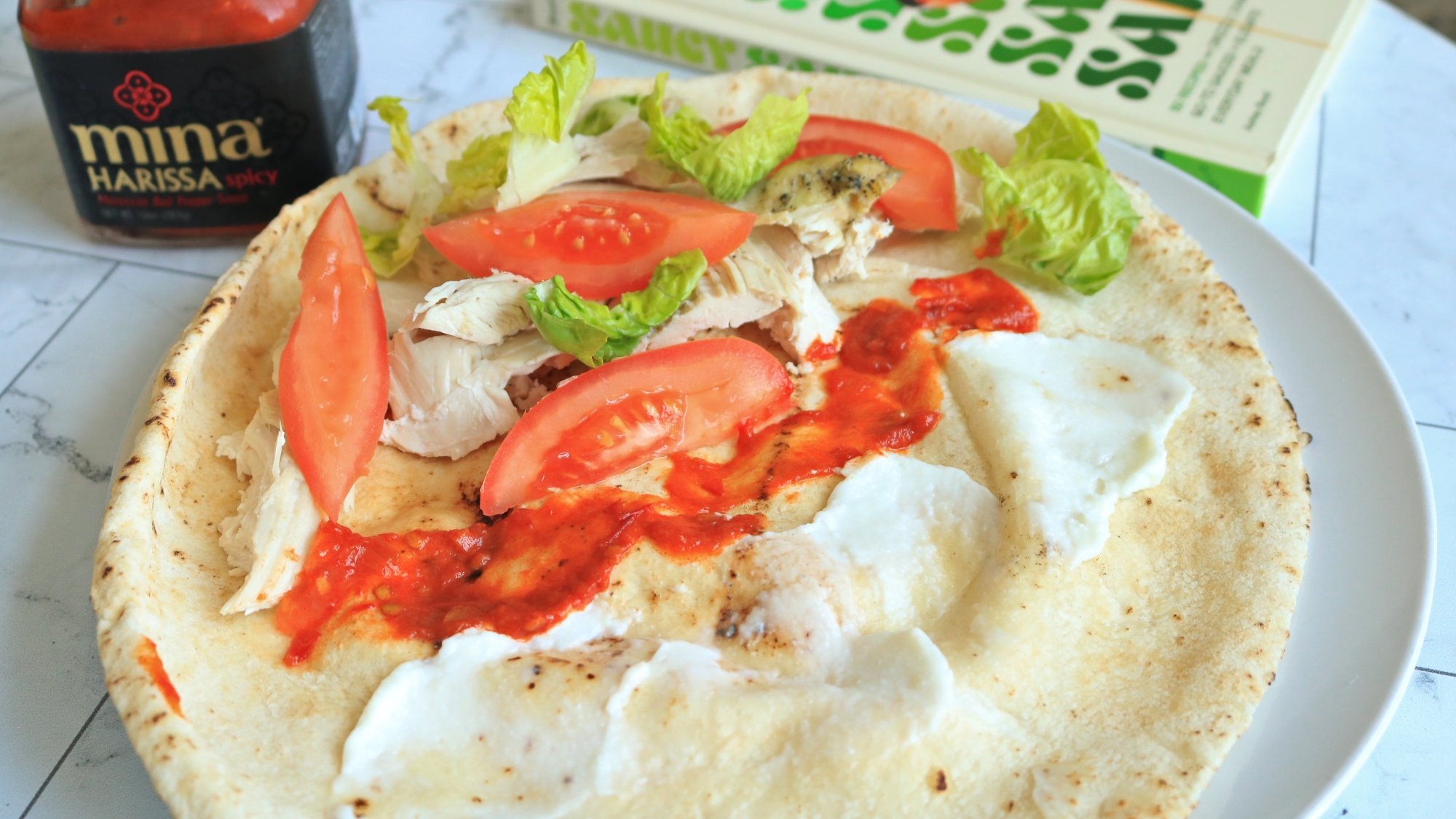 An open pita with garlic sauce, hot sauce, lettuce, and chicken.