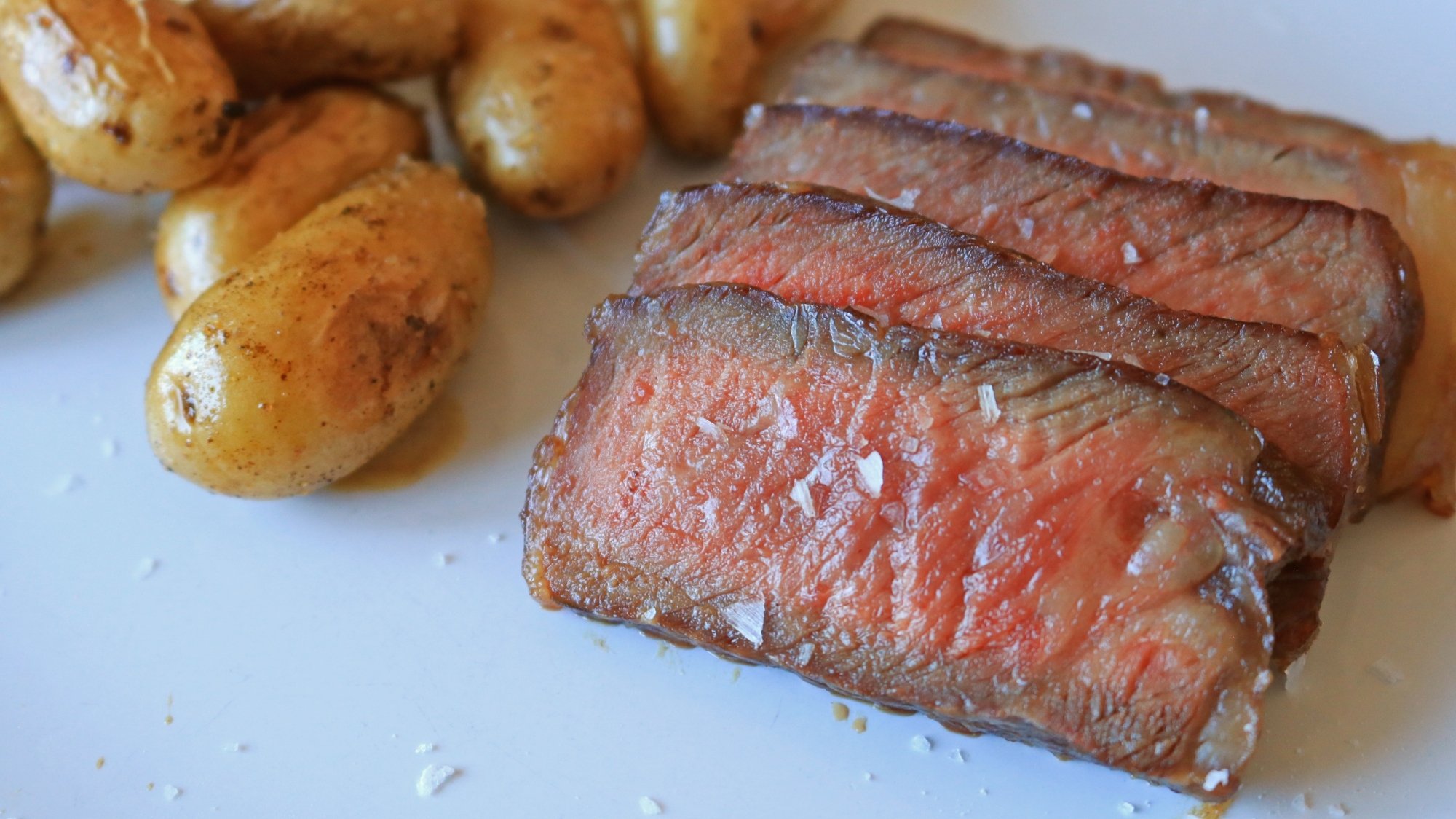 Steak sliced on a plate with small gold potatoes.