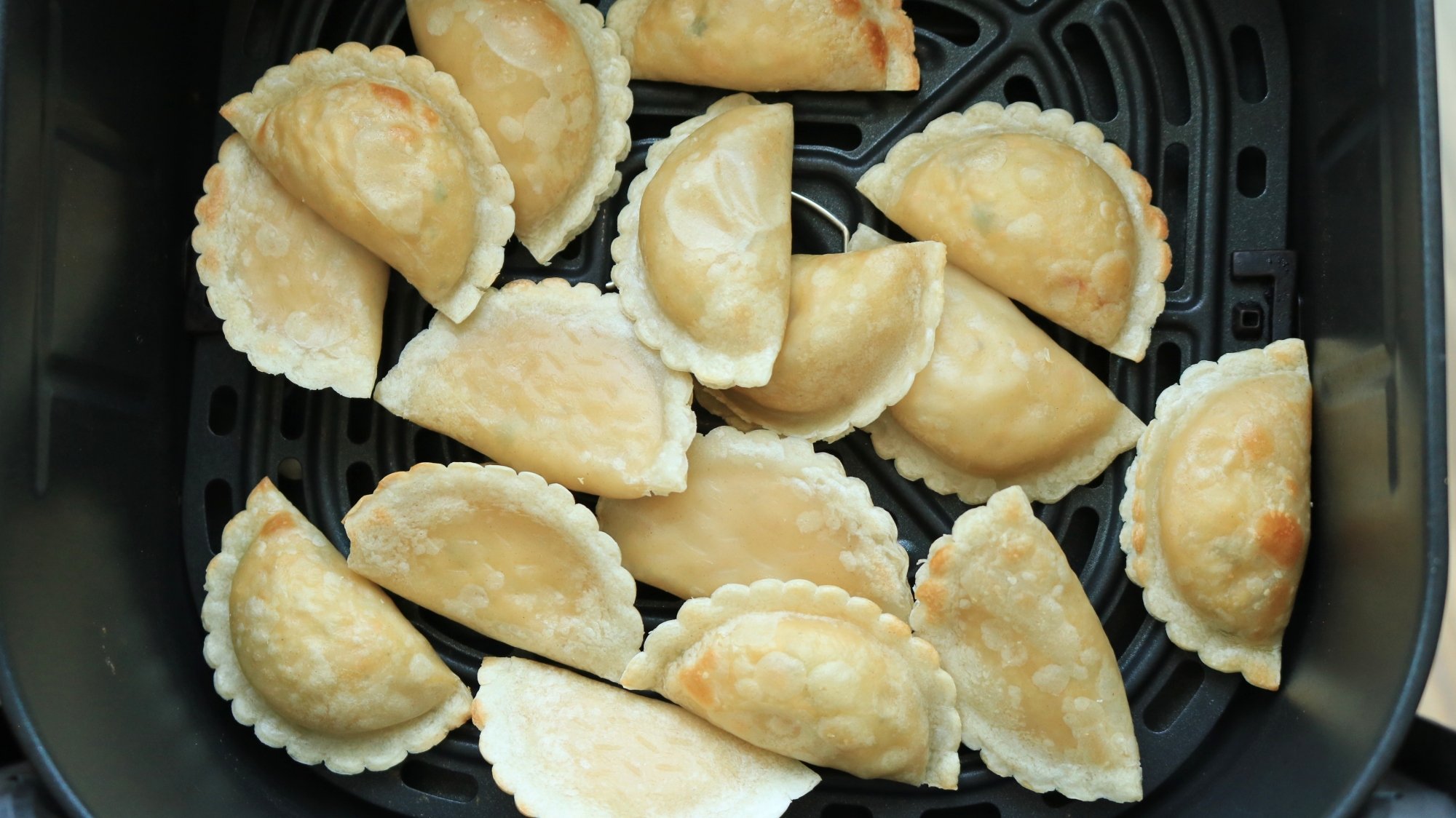 Many dumplings crowded together in an air fryer basket.