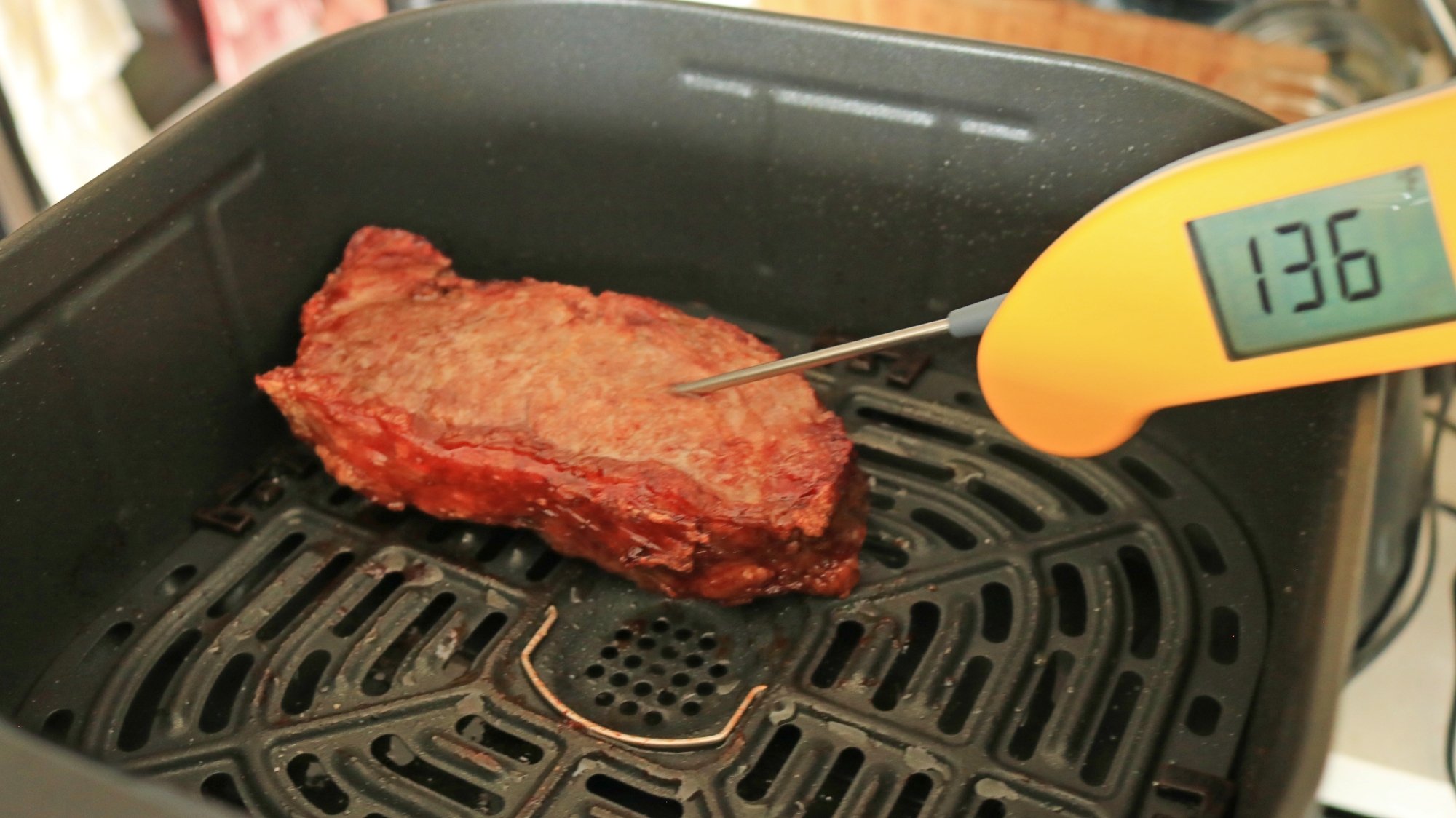 A digital thermometer testing the temperature of a steak in an air fryer basket.