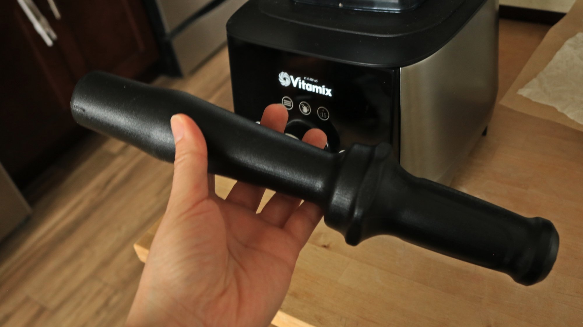 A hand holding a plastic tamper for the Vitamix blender.