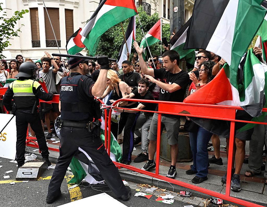 TOPSHOT - Basque regional police 'Ertzaintza' officer lifts a truncheon as pro-Palestinian protesters holding Palestinian flags demonstrate during the eleventh stage of the Vuelta a Espana cycling tour, a 167 km race from Bilbao to Bilbao, on September 3, 2025. (Photo by ANDER GILLENEA / AFP) (Photo by ANDER GILLENEA/AFP via Getty Images)