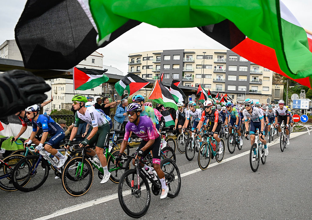 Pro-Palestinian protesters wave flags and shout as the peloton rides by in Poio at the start of the 16th stage of the Vuelta a Espana.