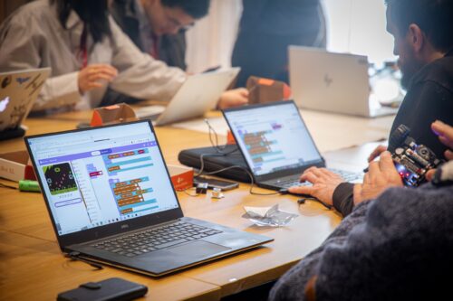 Educators collaborating on projects at a desk, with laptops open displaying a block-based coding environment.