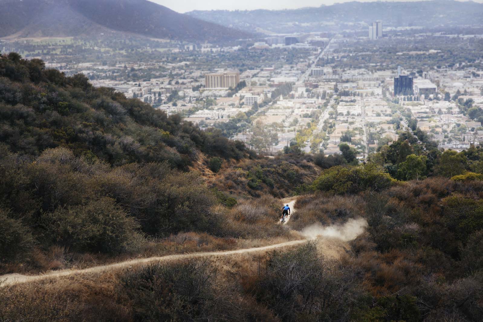 Person riding down mountain bike trail with city in background.