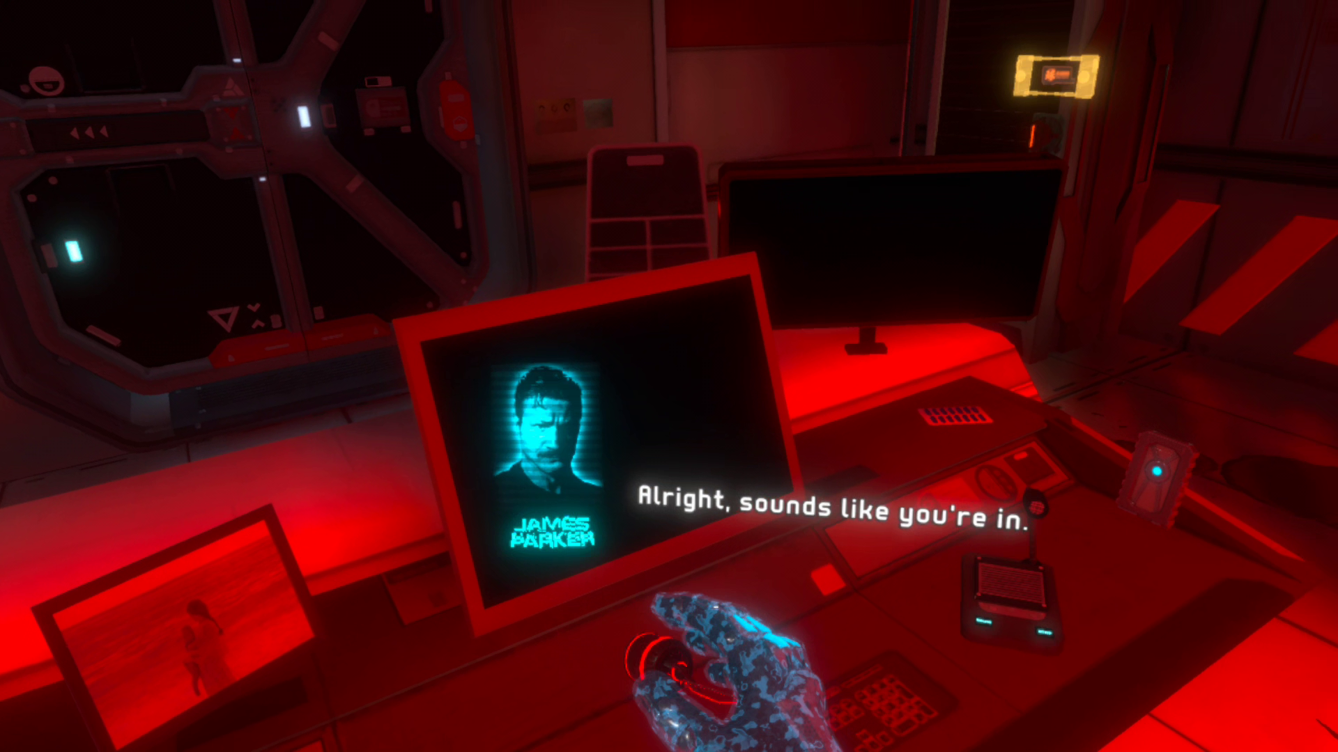 A blue hologram of a man named "James Parker" appears alongside the subtitles "Alright, sounds like you're in." as the player navigates a dimly lit personal office cast in a crimson hue.
