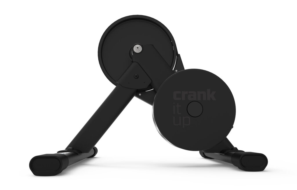 A black stationary bike trainer with two wide, angled legs and a large circular flywheel; the words crank it up are printed on the side. The image has a clean, white background.