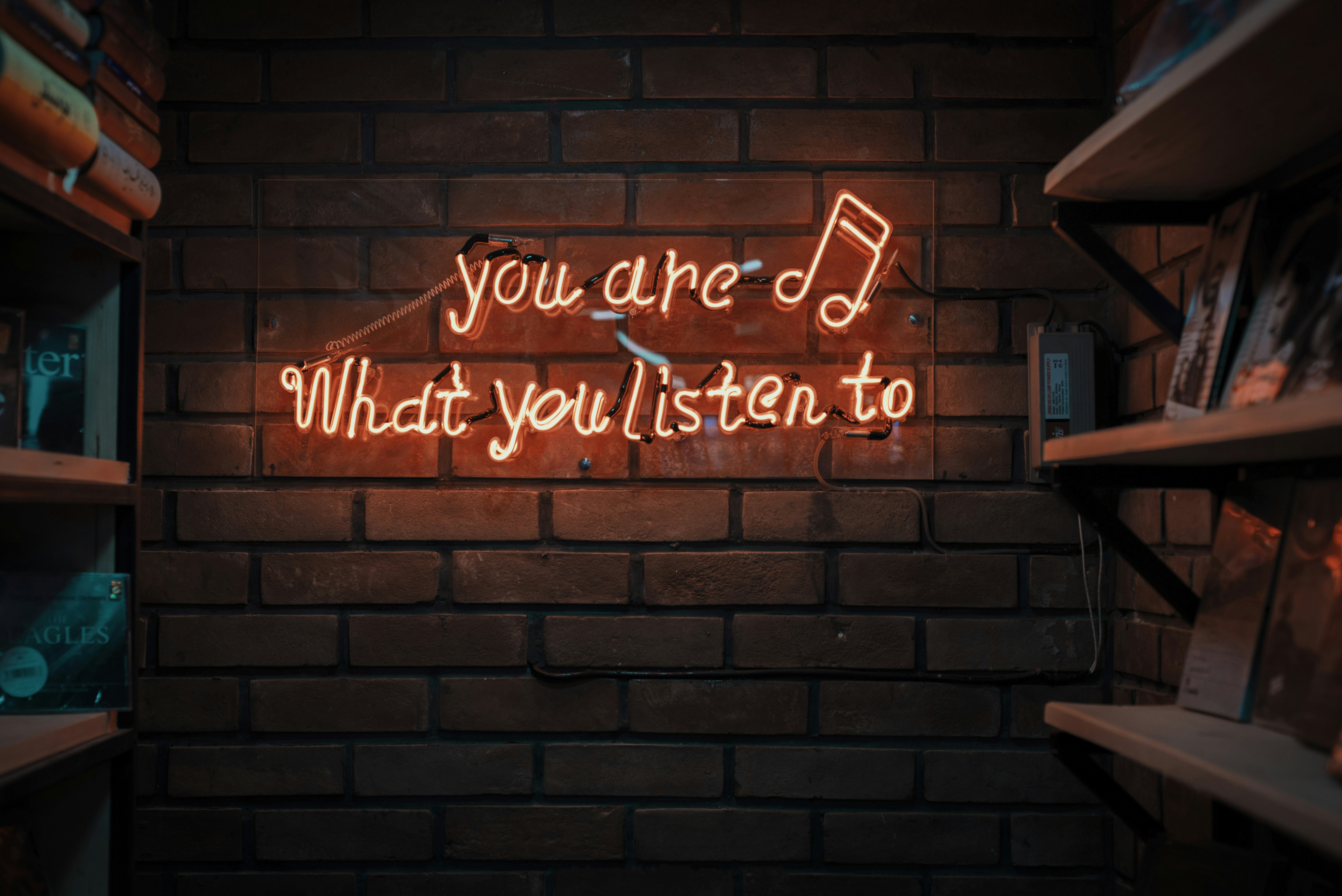 A neon sign on a wall, reading, "You are what you listen to."