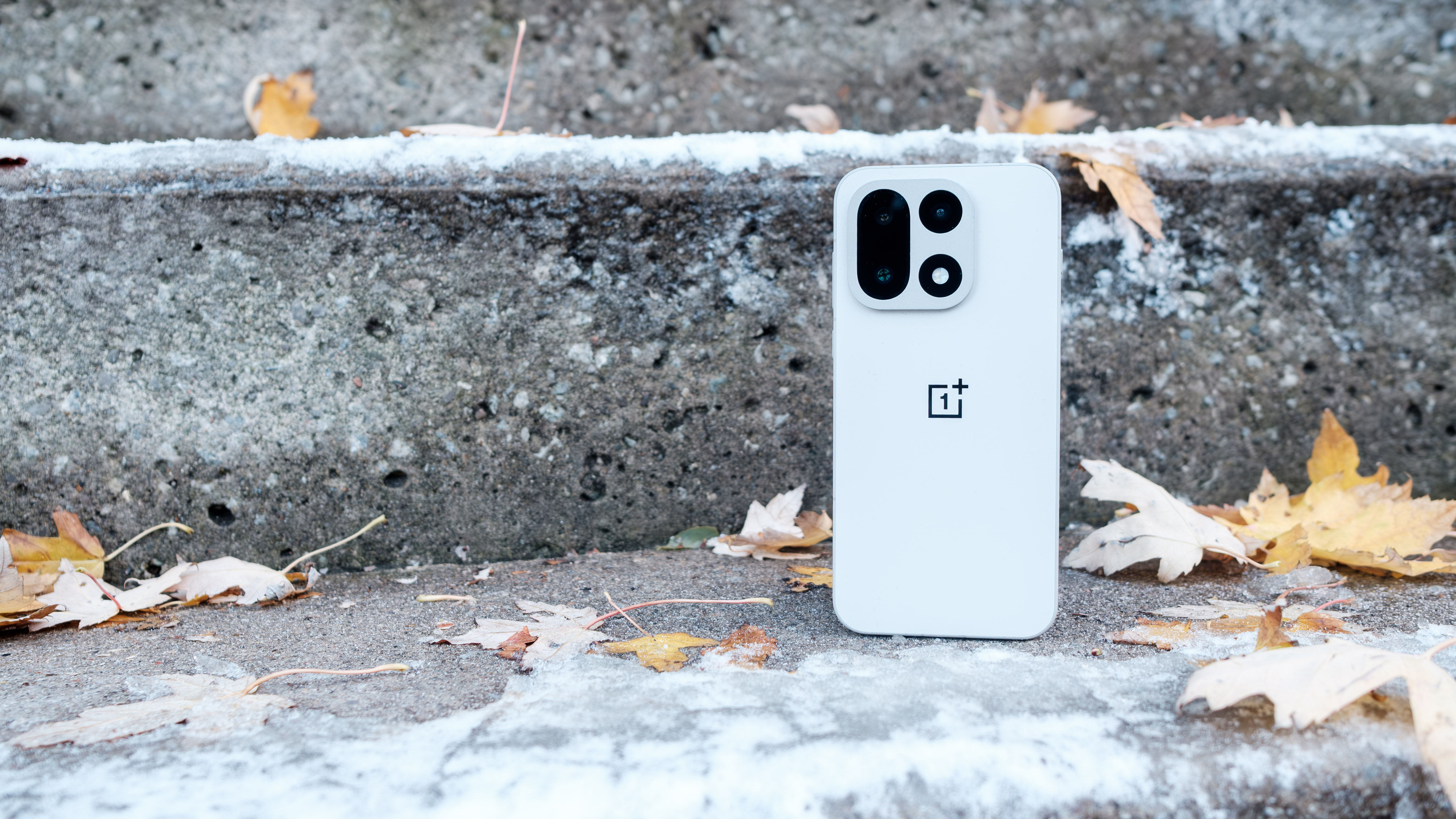 The OnePlus 15 sits on a set of icy concrete steps. 