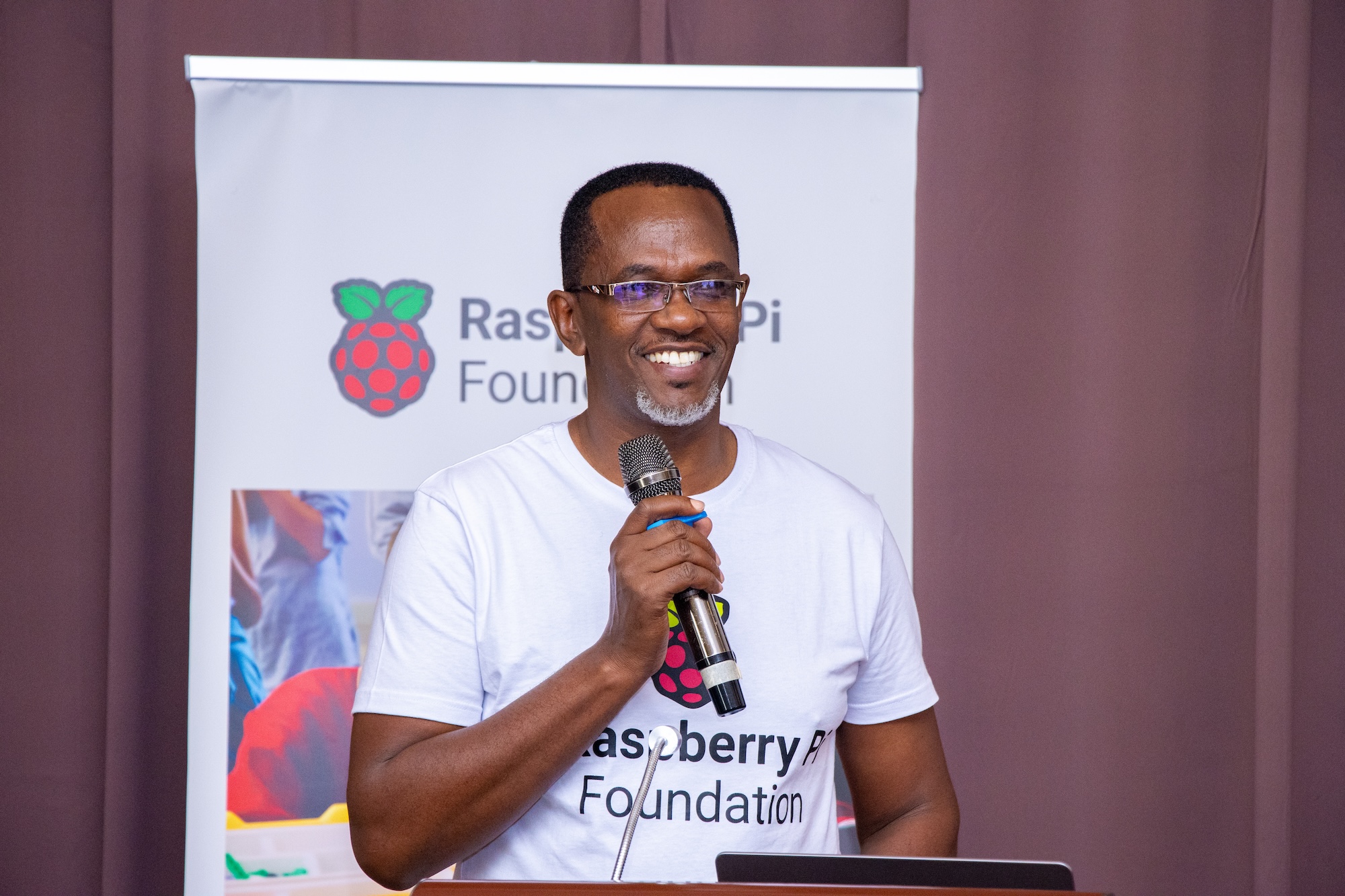 A speaker at the Raspberry Pi Foundation's Kenya Partner Showcase 2025, smiling and holding a microphone.