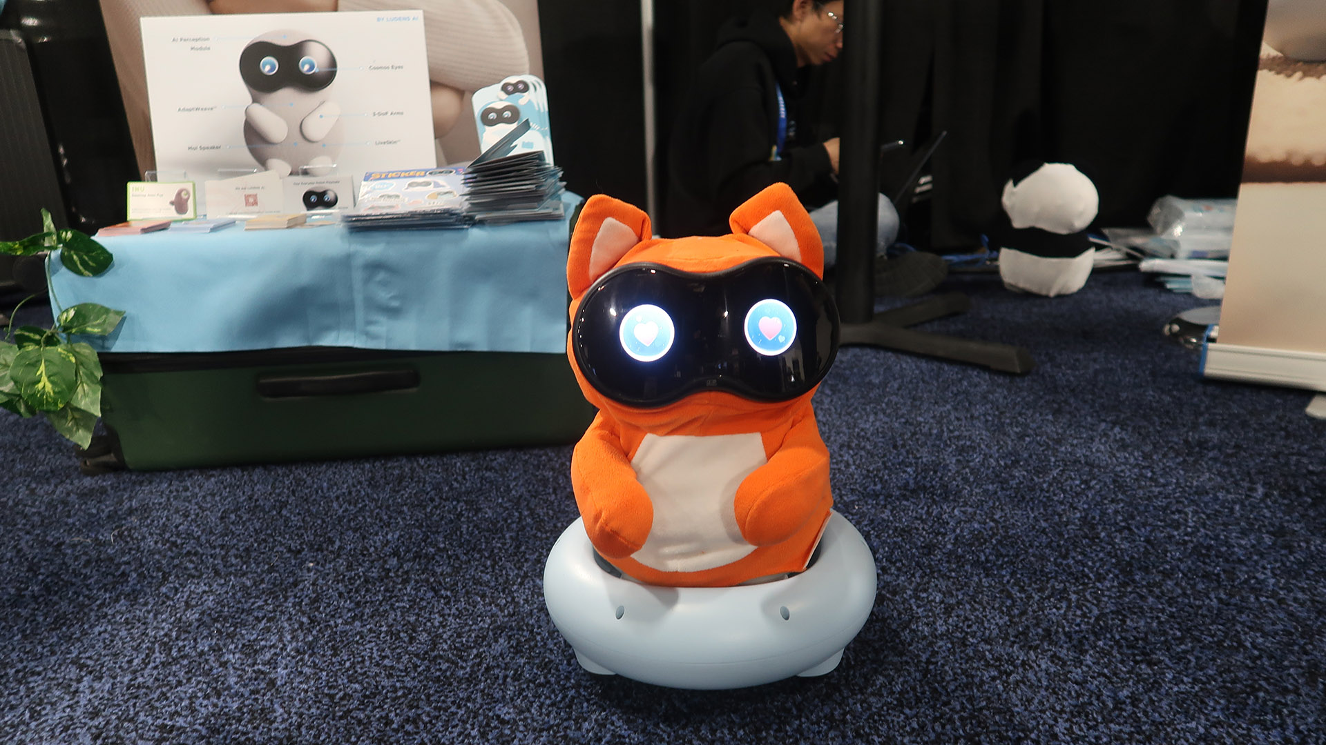 An orange, egg-shaped robot with a black face hearts in its eyes sitting on a wheeled base.