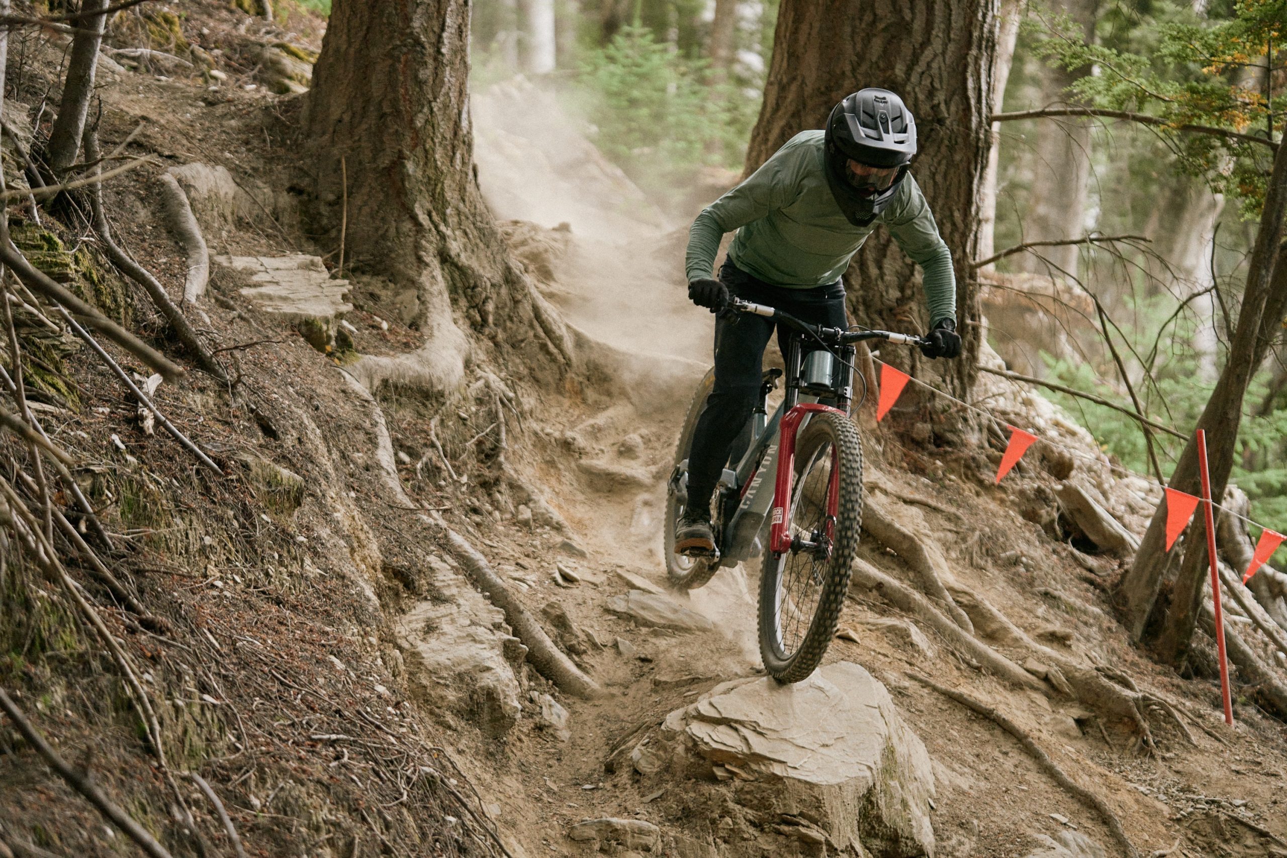 Rider on downhill bike in full face helmet riding down a rocky and rooty track in Queenstown, New Zealand.
