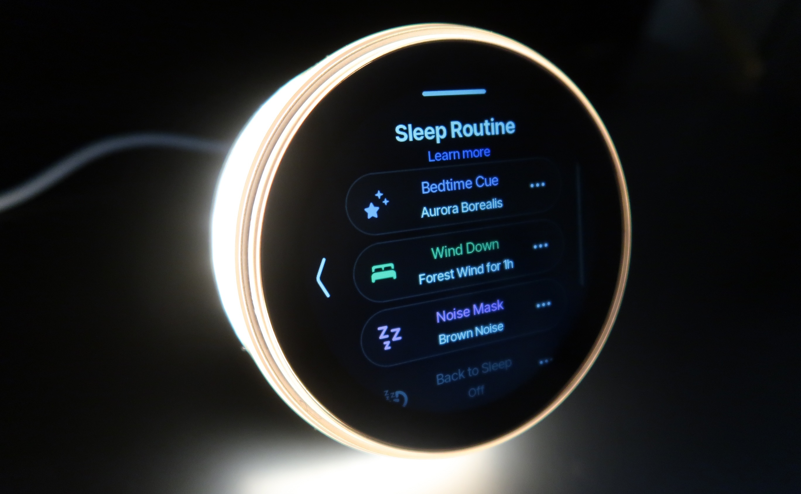 Dreamie alarm clock with its light ring on, and the screen displaying a sleep routine: Bedtime Cue, Wind Down, and Noise Mask