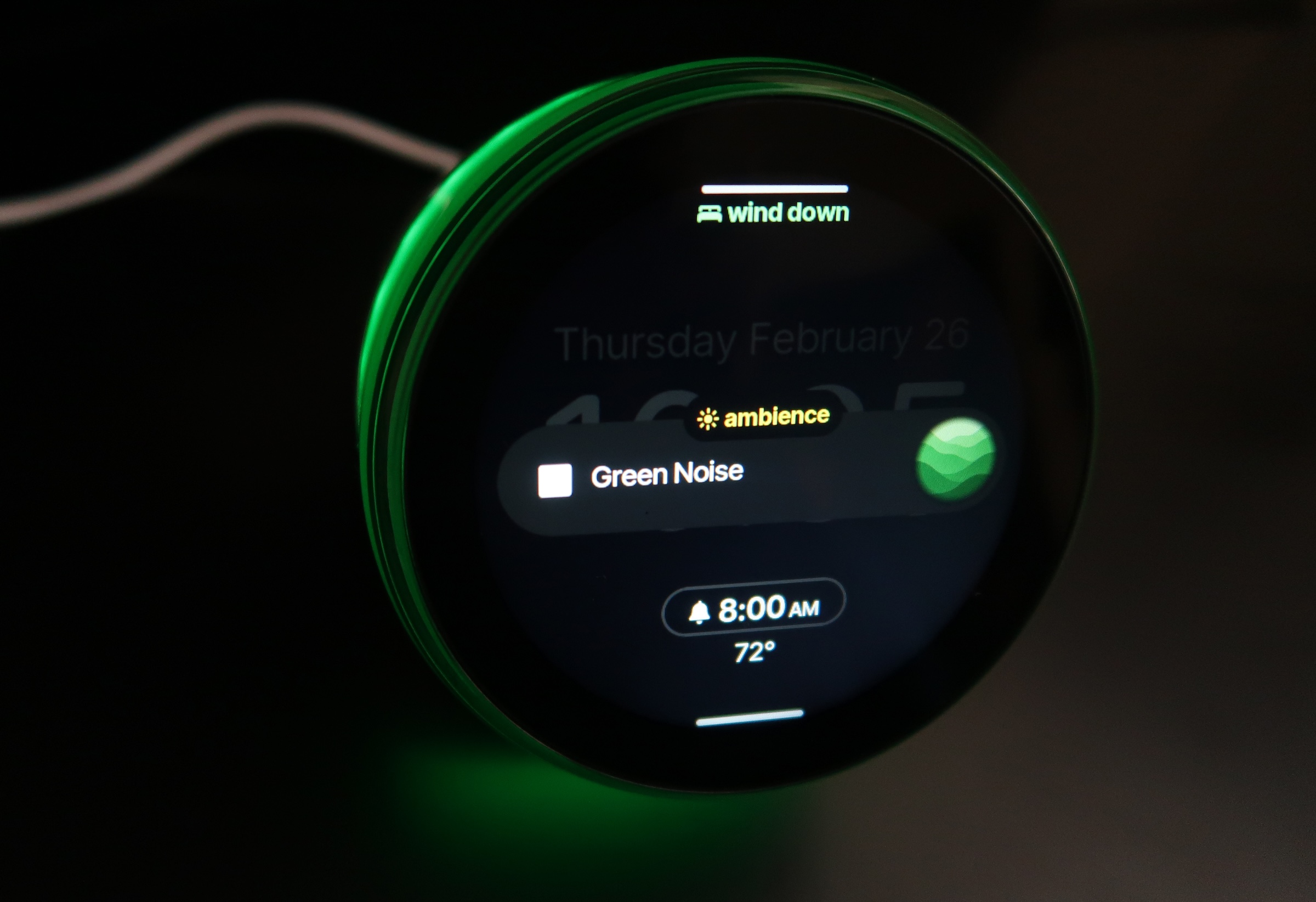 A Dreamie clock is shown with a ring of green light coming from around its display. The screen shows that it is in ambience mode, with Green Noise playing