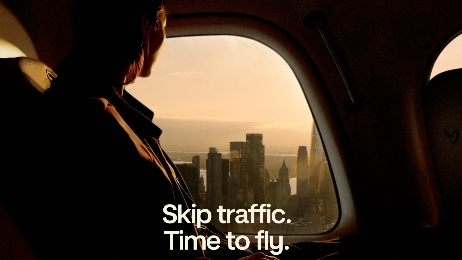 A person looks out the window of an air taxi, viewing the city below.