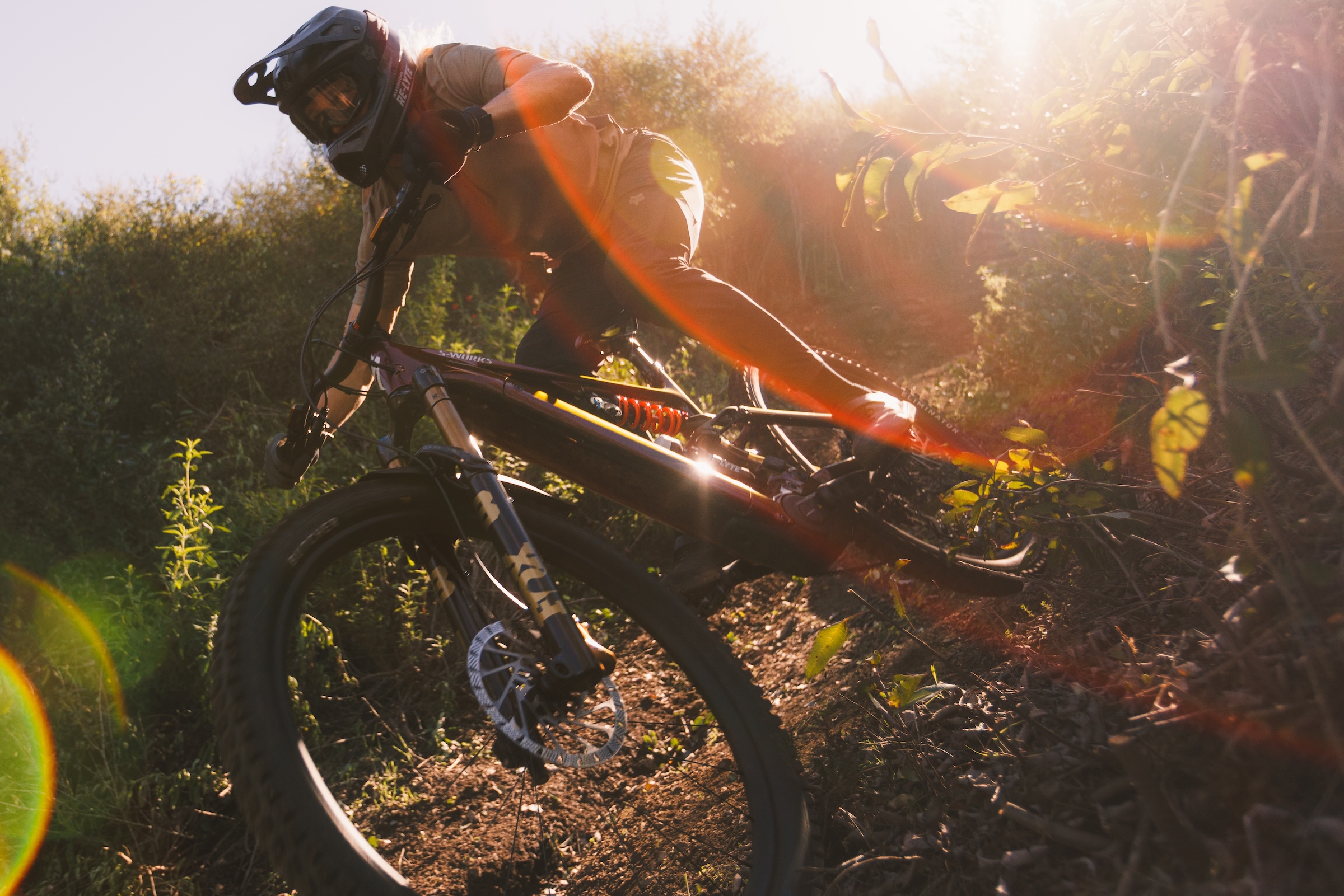 Mountain biker riding fast through narrow trail with Fox 38 fork in low sunlight