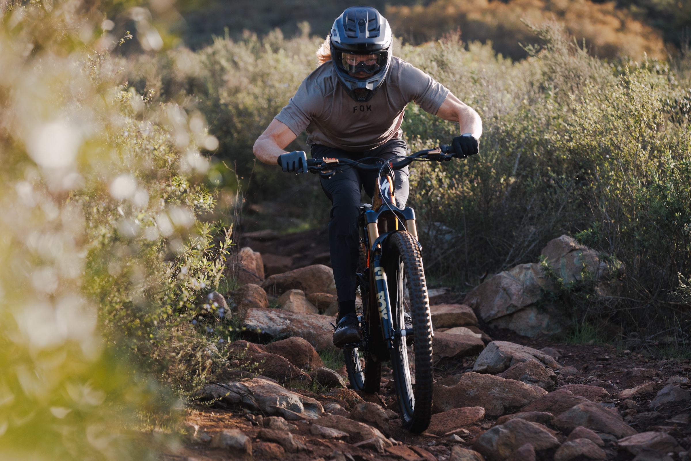 Mountain biker riding rocky trail with Fox 38 suspension fork compressing over uneven terrain