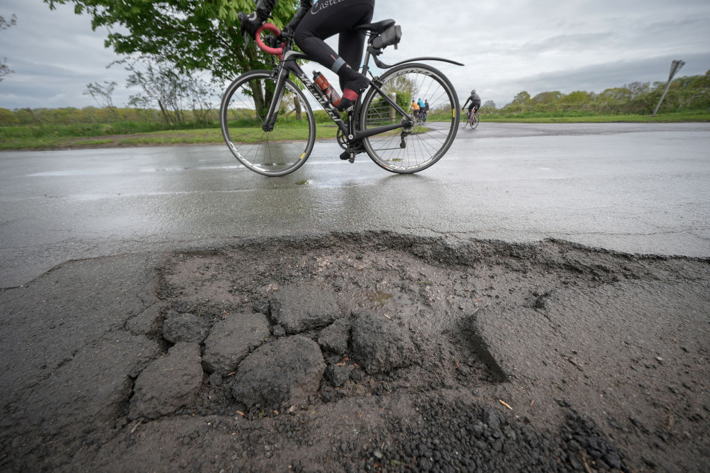 A cyclist rides past a pothole on the road.