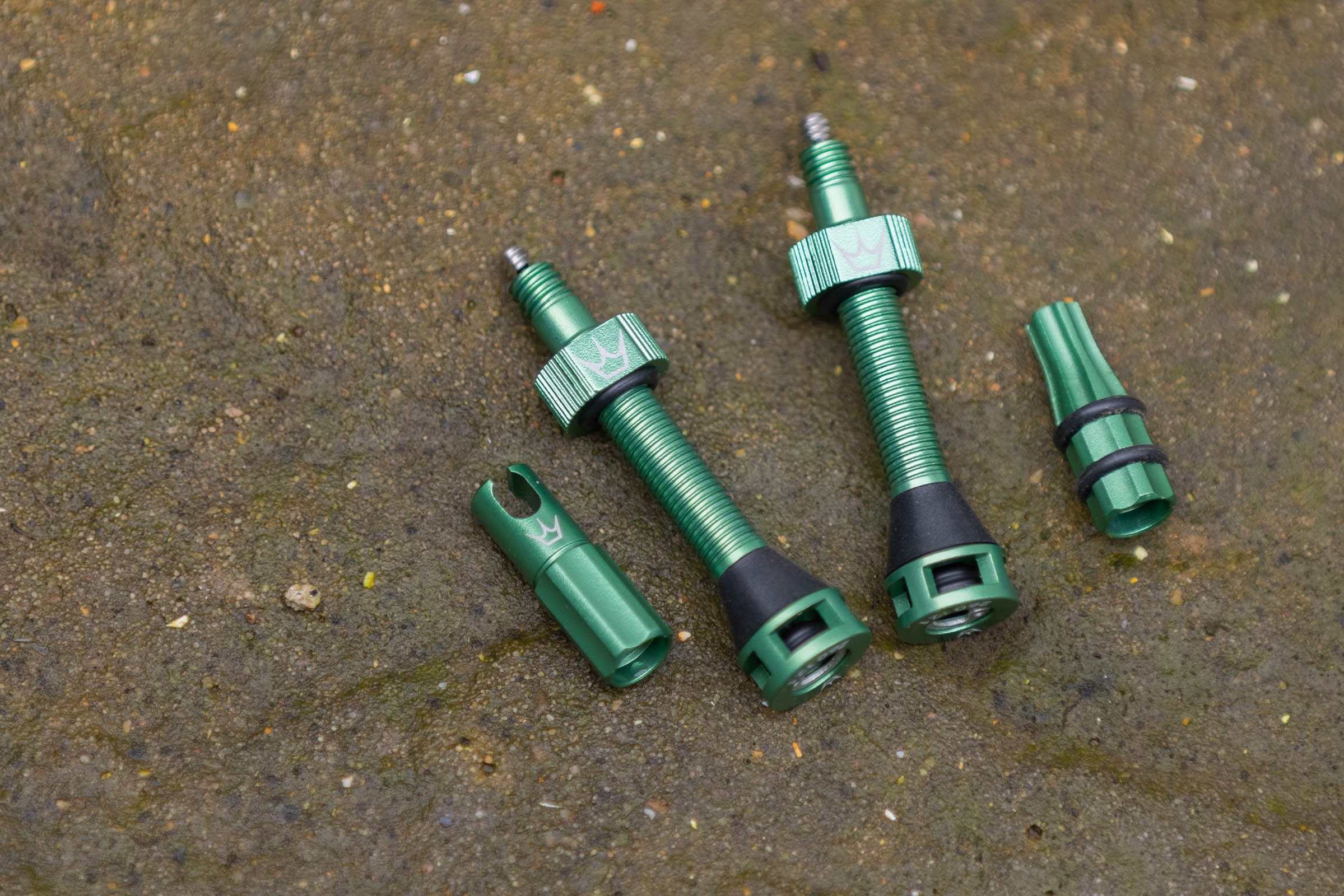 Peaty's Holeshot Fast Flow valves with valve caps off and next to them on a stone surface.